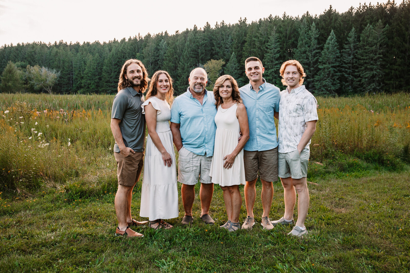 Mom and dad stand with their 4 adult children in an open field with wildfowers