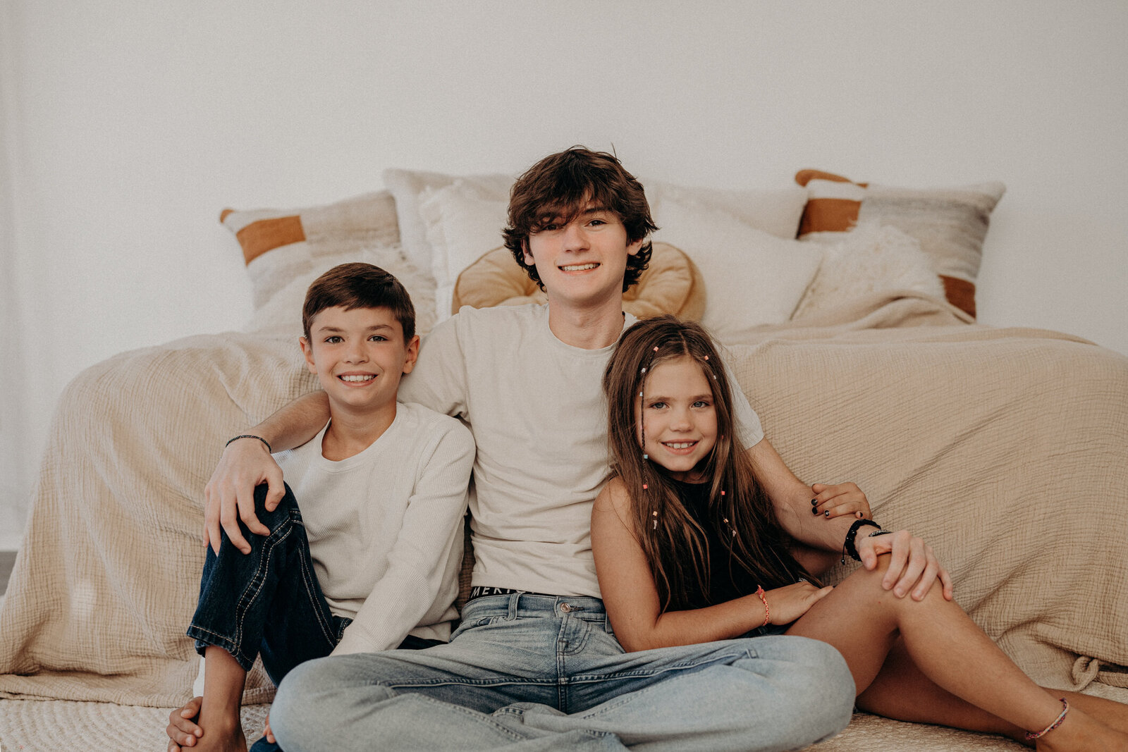 Three siblings sit on the floor, smiling towards the audience