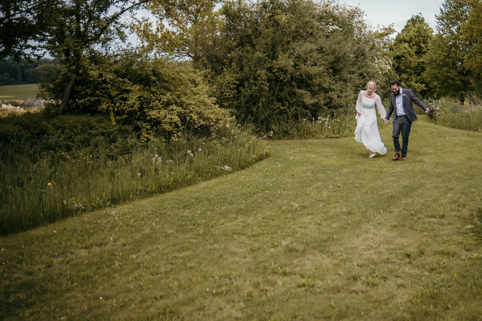 Das Foto vom Paarshooting zeigt das Hochzeitspaar über eine Wiese laufend und tanzend.