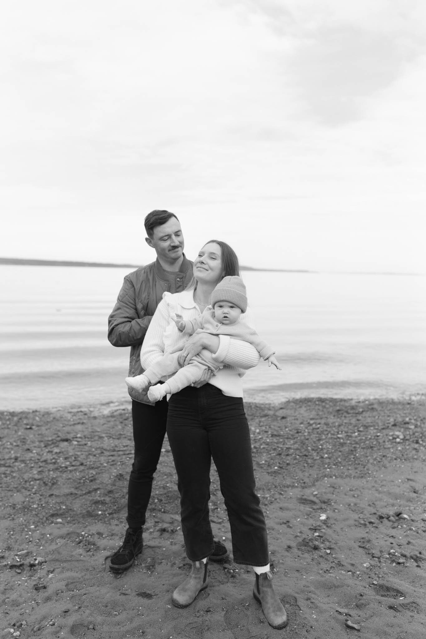 Mother holding baby and father holding mother at the beach on the Oregon Coast.