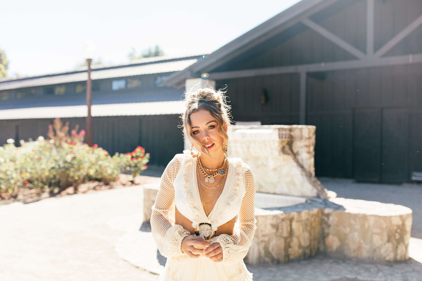 brunette girl wearing white outfit and gold jewelry standing in front of home