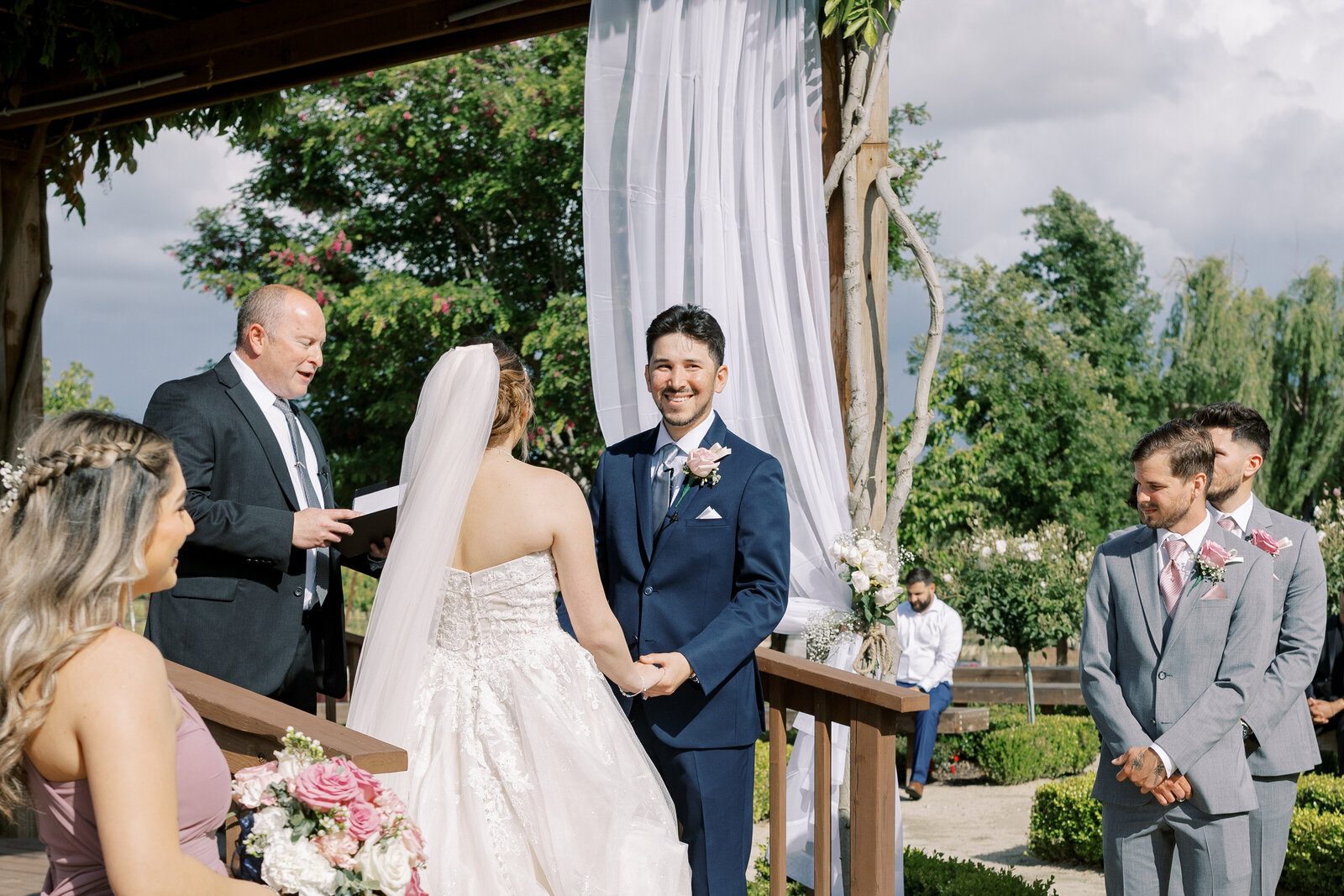 sacramento wedding photographer photographs shot of groom during their wedding ceremony as he laughs while reading his vows at an outdoor Bay Area wedding venue