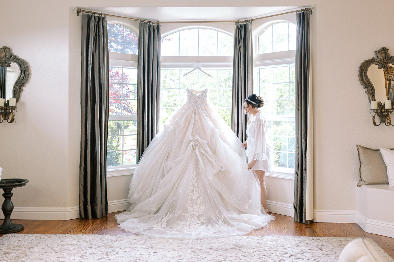 bride holding her ballgown wedding dress in a bay window of her bridal suite at a bay area wedding venue captured by sacramento wedding photographer