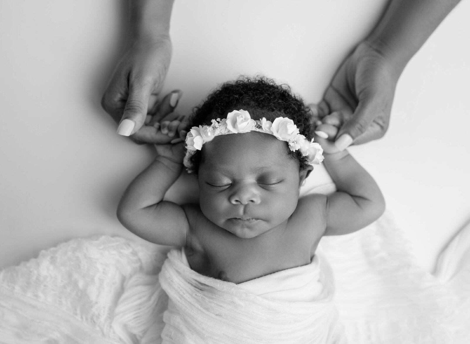 B&W newborn photo of baby sleeping and Mom holding her hands.