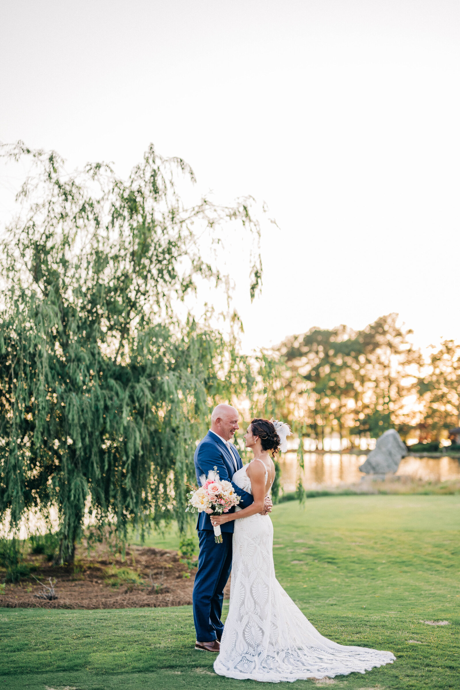 Man in blue suit holding woman in white dress while she is holding a bouquet of pink flowers 