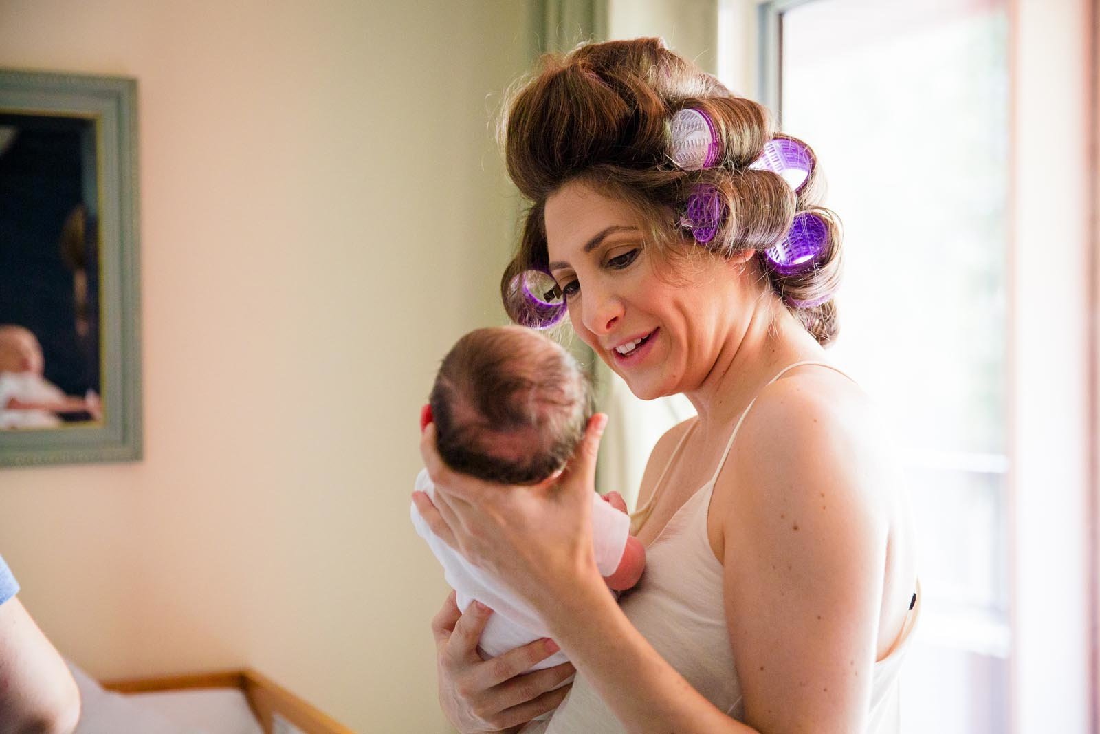 mom in hair rollers looking lovingly at her newborn son in her hands