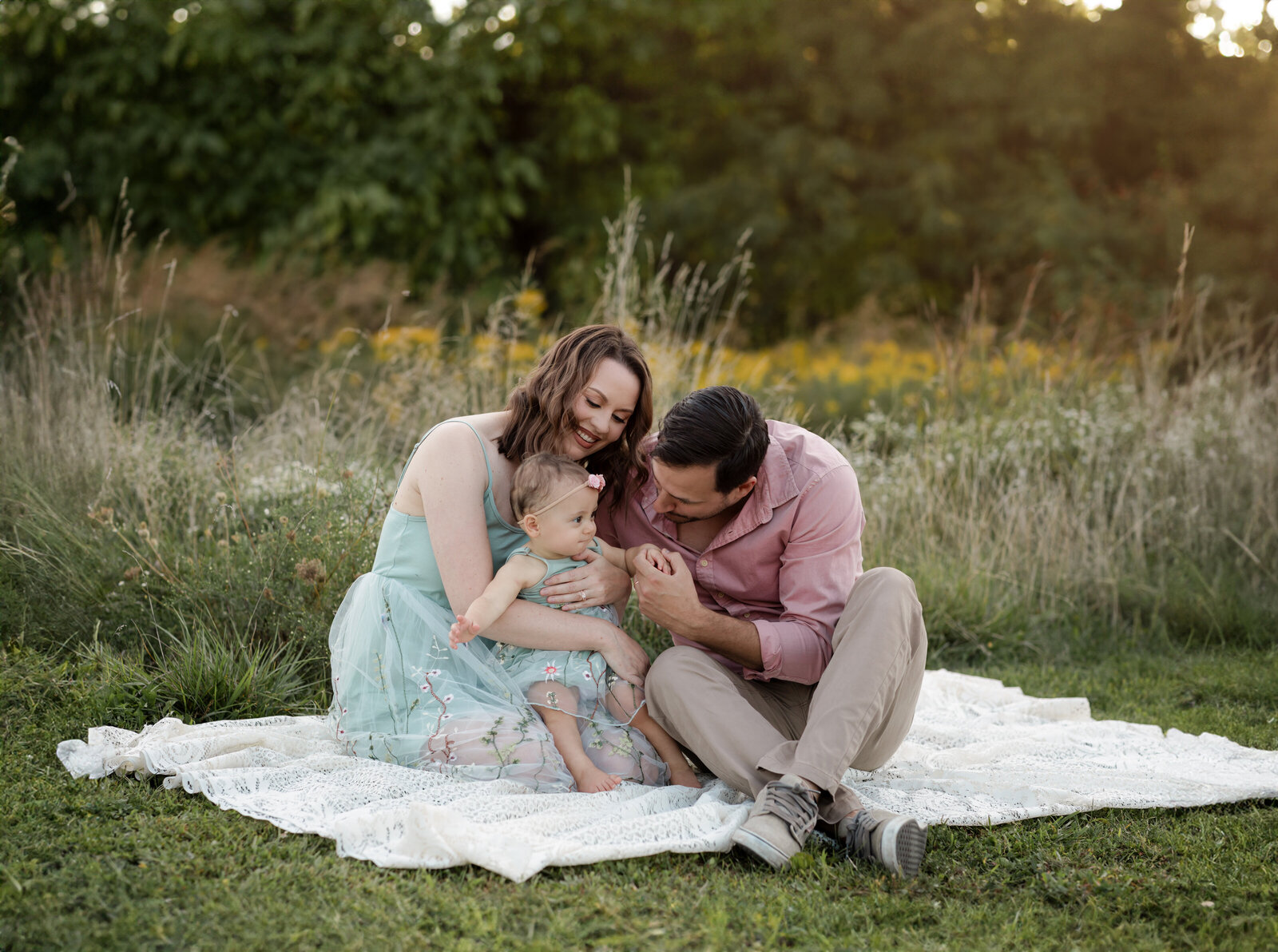 mom and dad sitting on ground holding daughter for family photos 