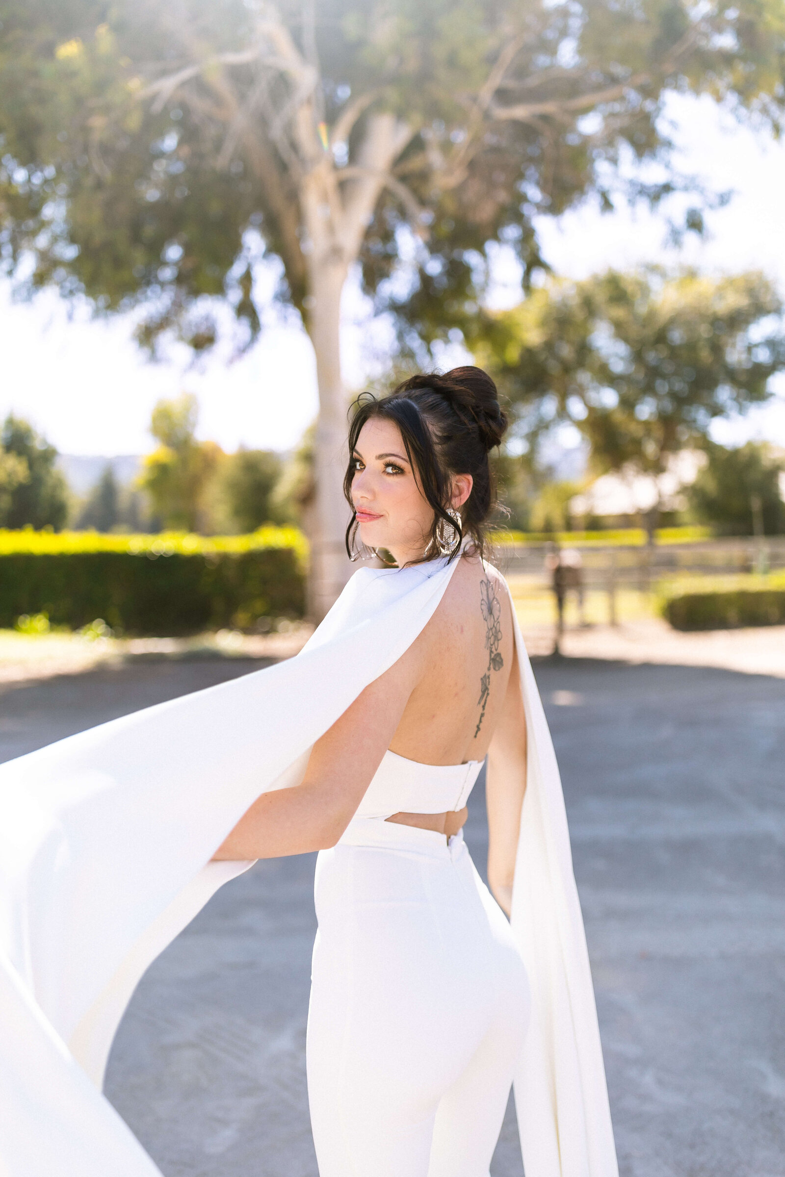 girl with dark hair and a back tattoo wearing a romper with flowy white sleeves posing