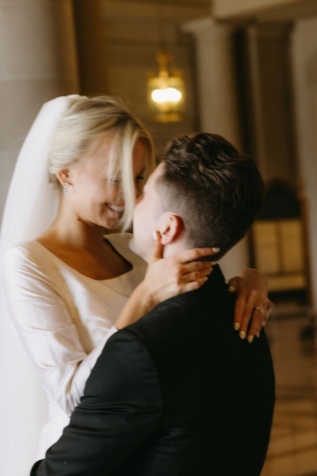 A newlywed couple sharing a tender moment during their elopement photoshoot in San Francisco City Hall, with the bride pulling the groom closer for a kiss.