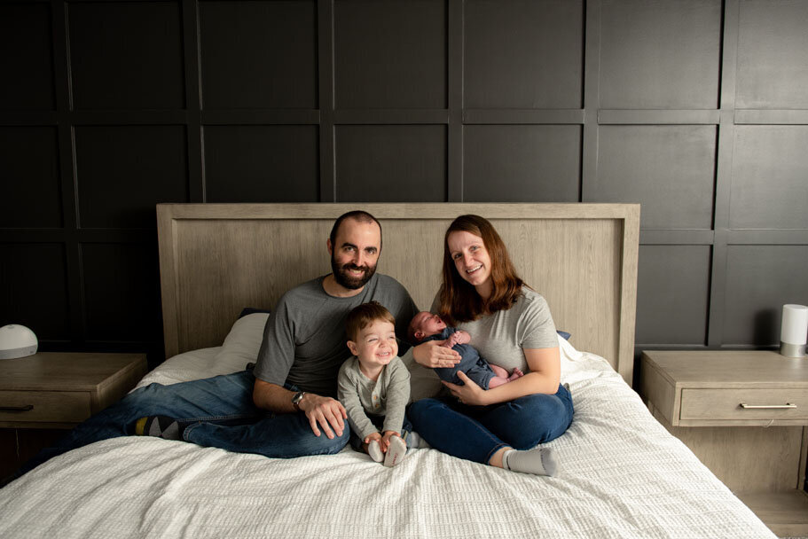 Troy Michigan family with newborn posing on the master bed smiling
