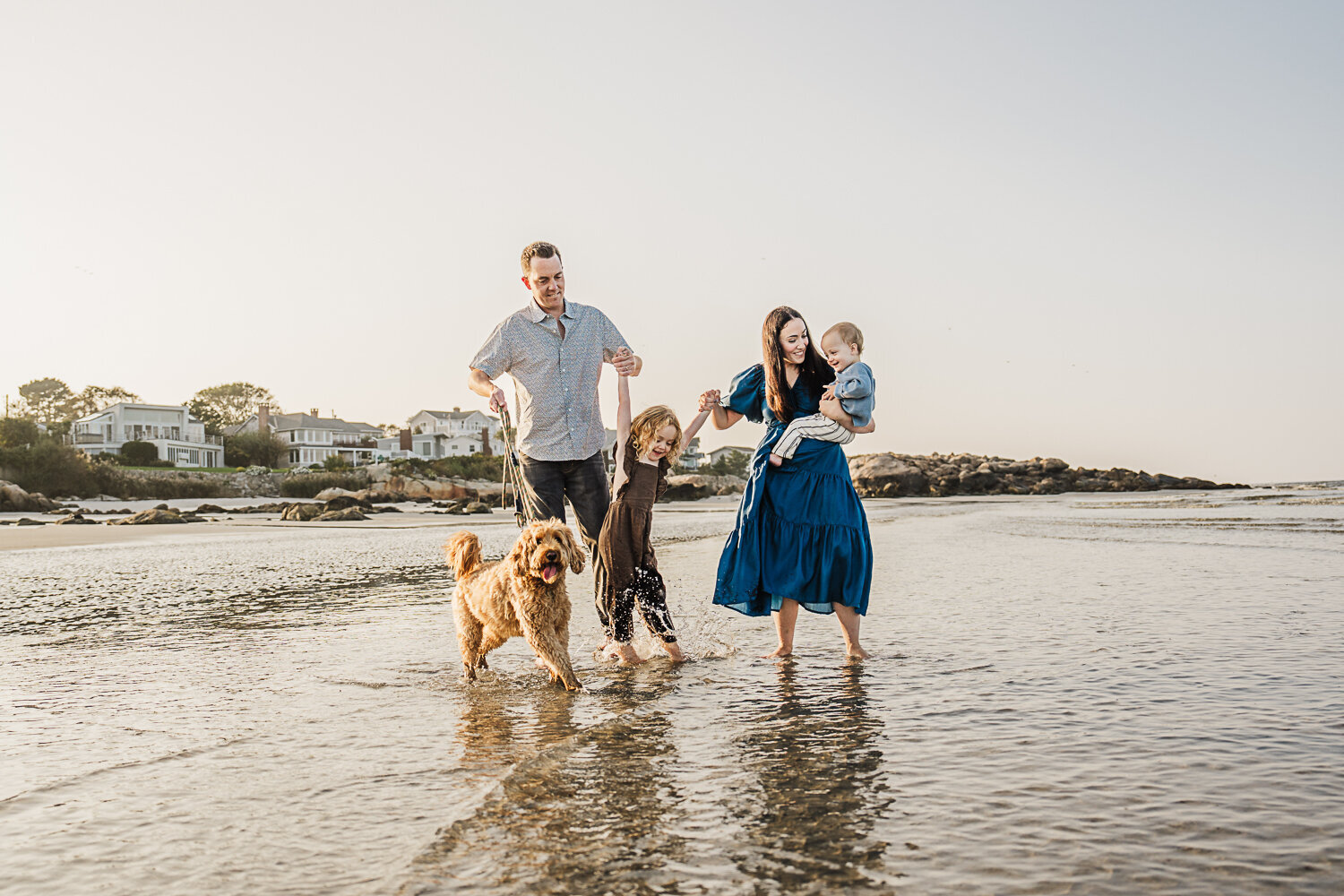 parents with two kids and a golden doodle play in the waves at beach