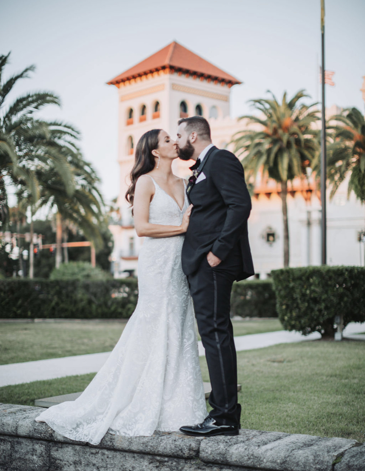 bride in white dress with dark hair  and groom  with brown hair and beard wearing a black tux standing outside in St. Augustine,, Florida enjoying a kiss