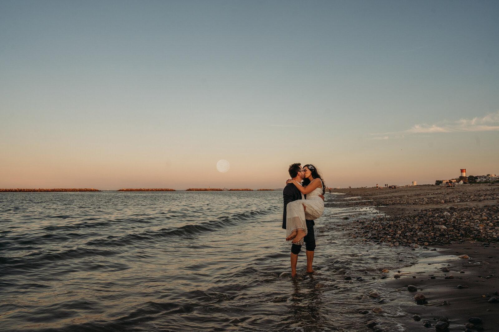 man picks up woman in ocean with moon behind them