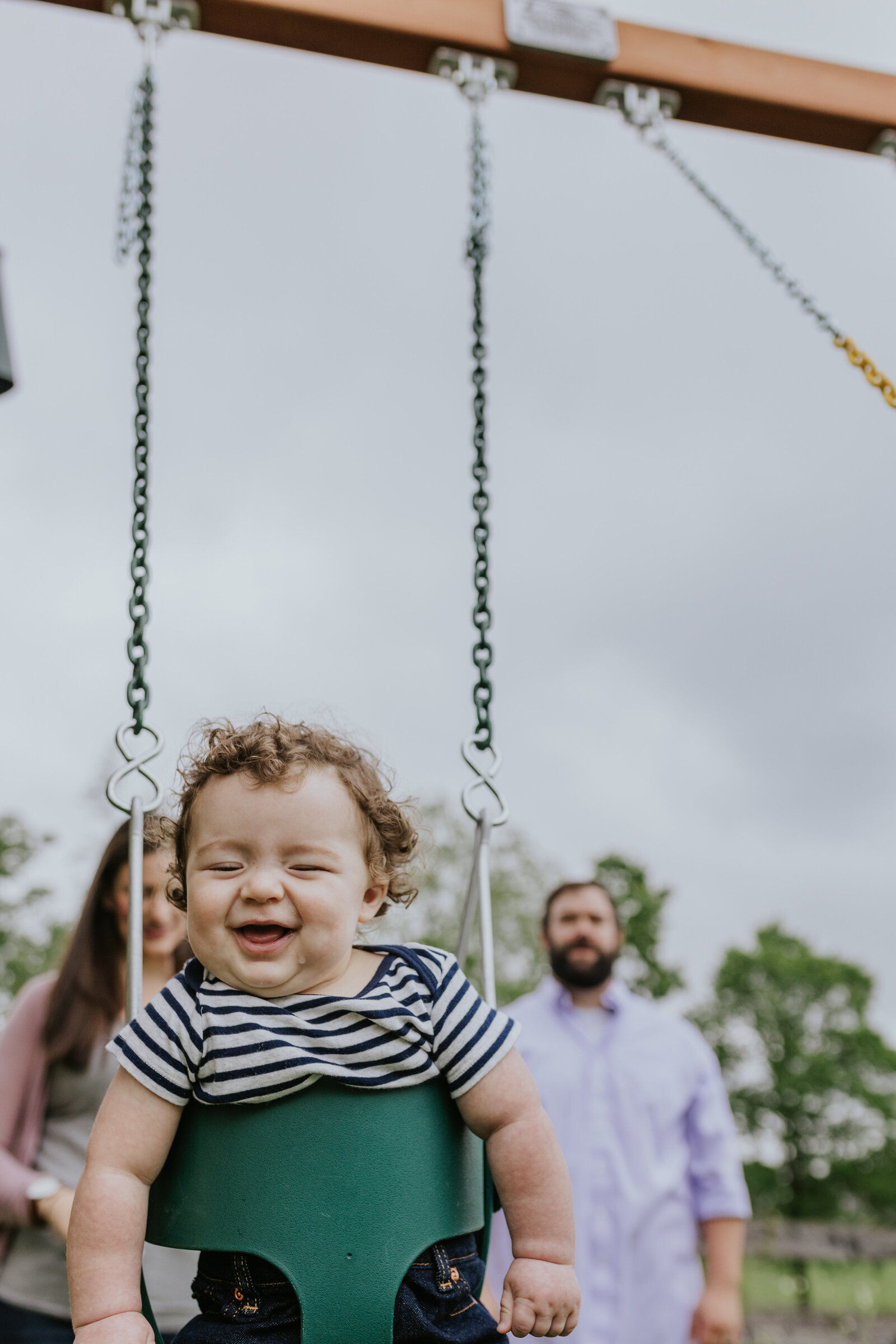 A mother and father push their laughing baby in a swing