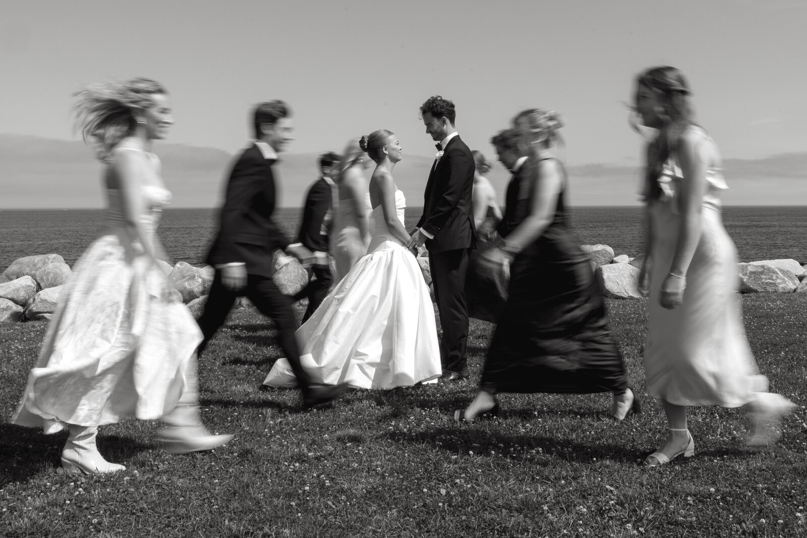 A bride and groom stand in the middle of a portrait in their wedding attire while their bridal party walks around them.