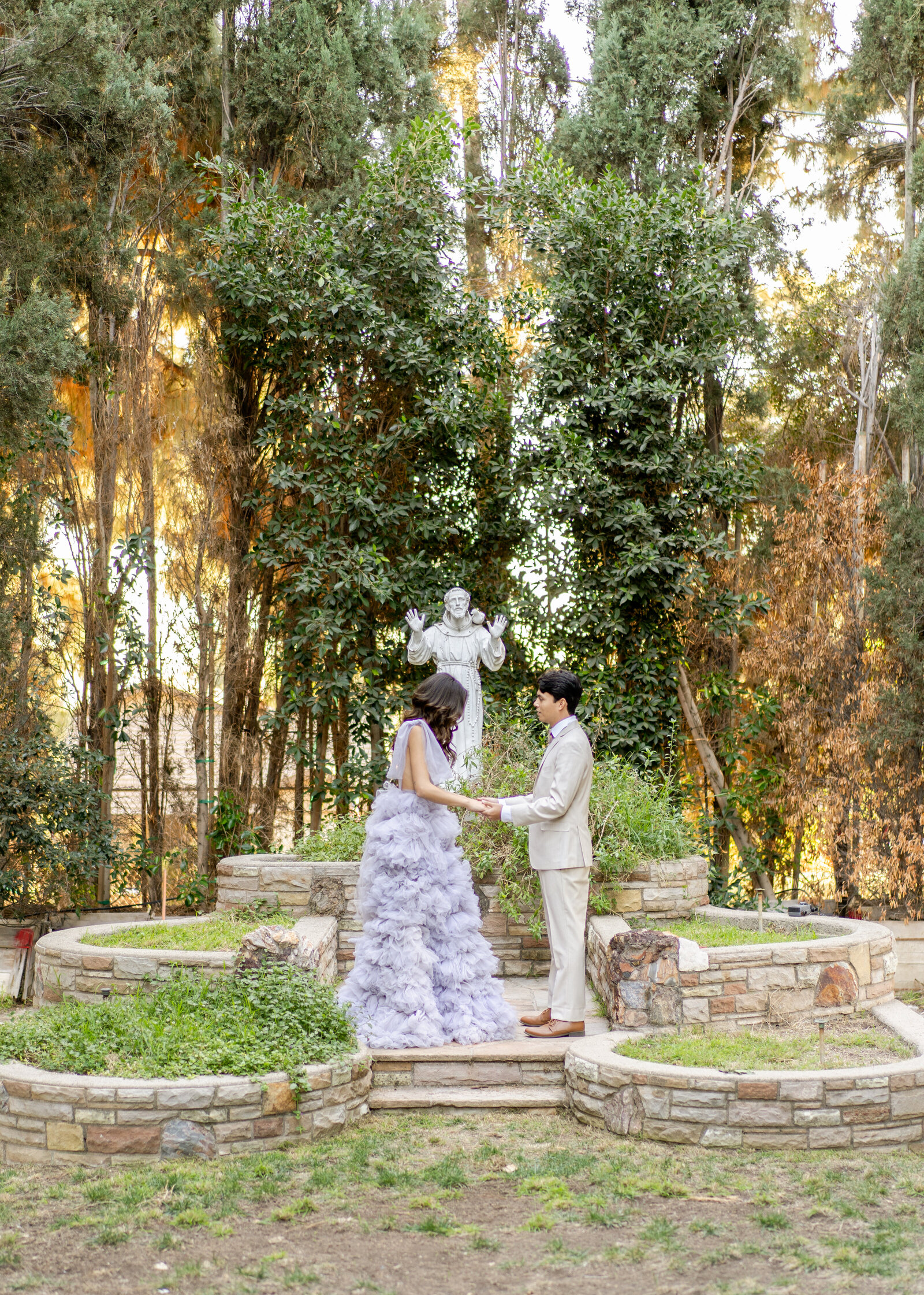 Portrait of a bride and groom in a lavender gown and cream suit with tress outback.
