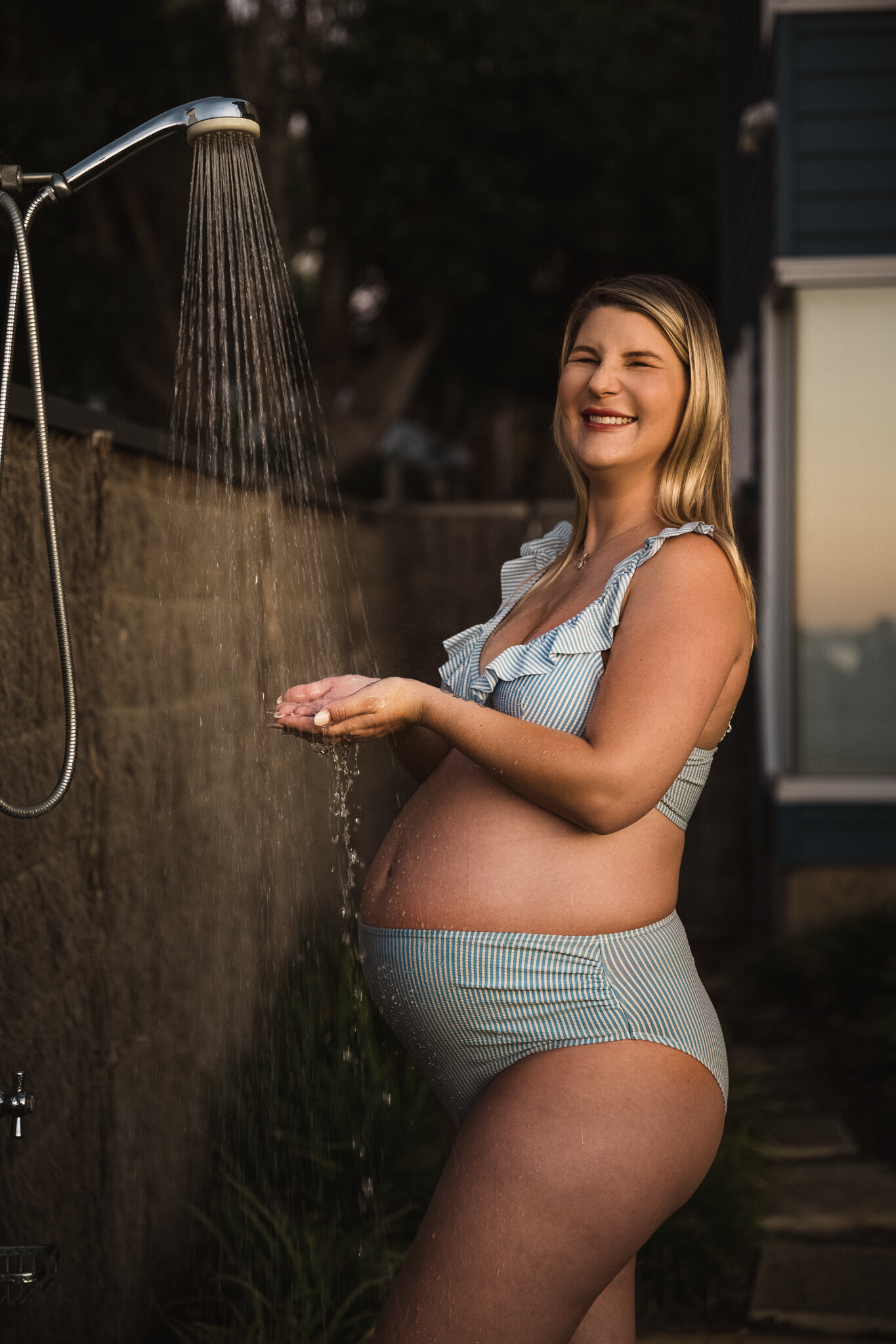 beautiful pregnant lady in front of a funning outdoor shower in the cutest blue bikini
