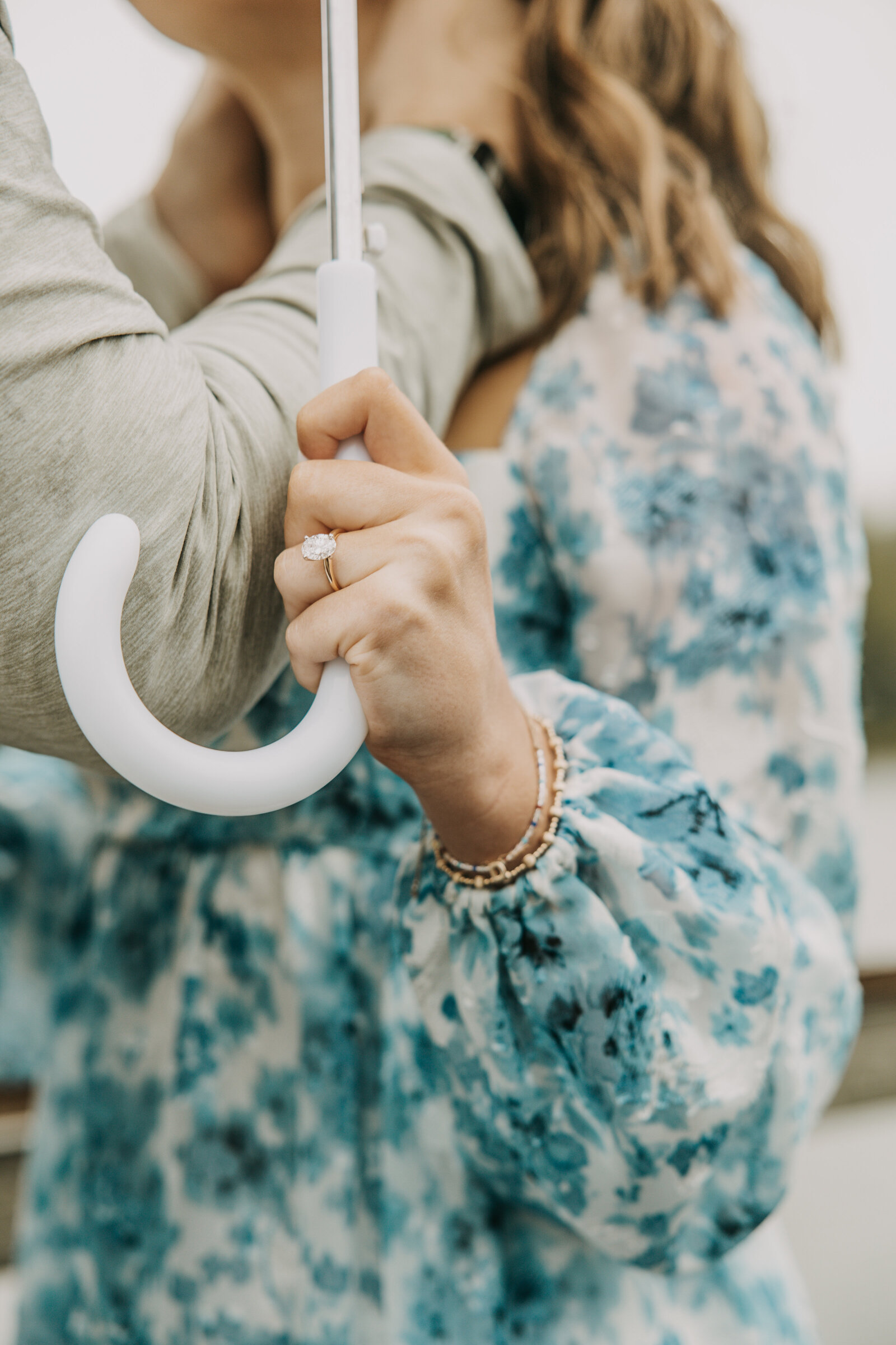 Close-up of a woman holding an umbrella on a rainy day, with a focus on her sparkling engagement ring.