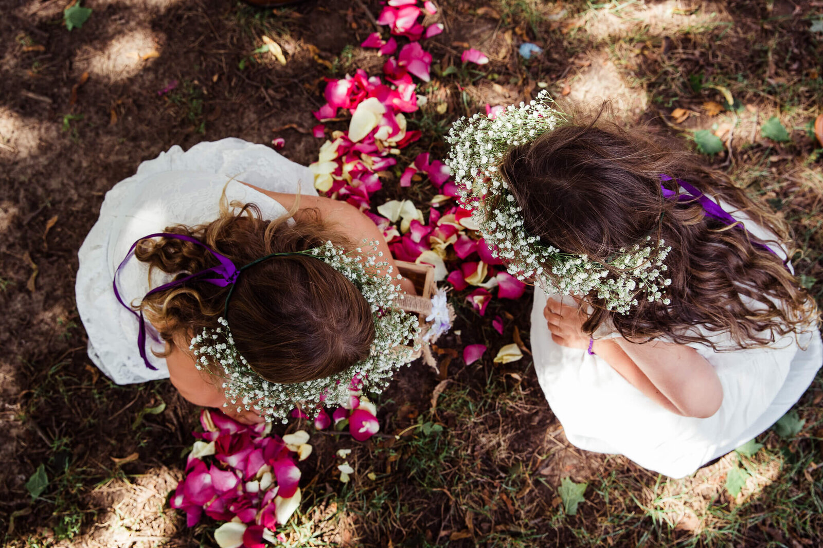 Two flower girls wearing floral crowns play with rose petals at Fanshawe Pioneer Village