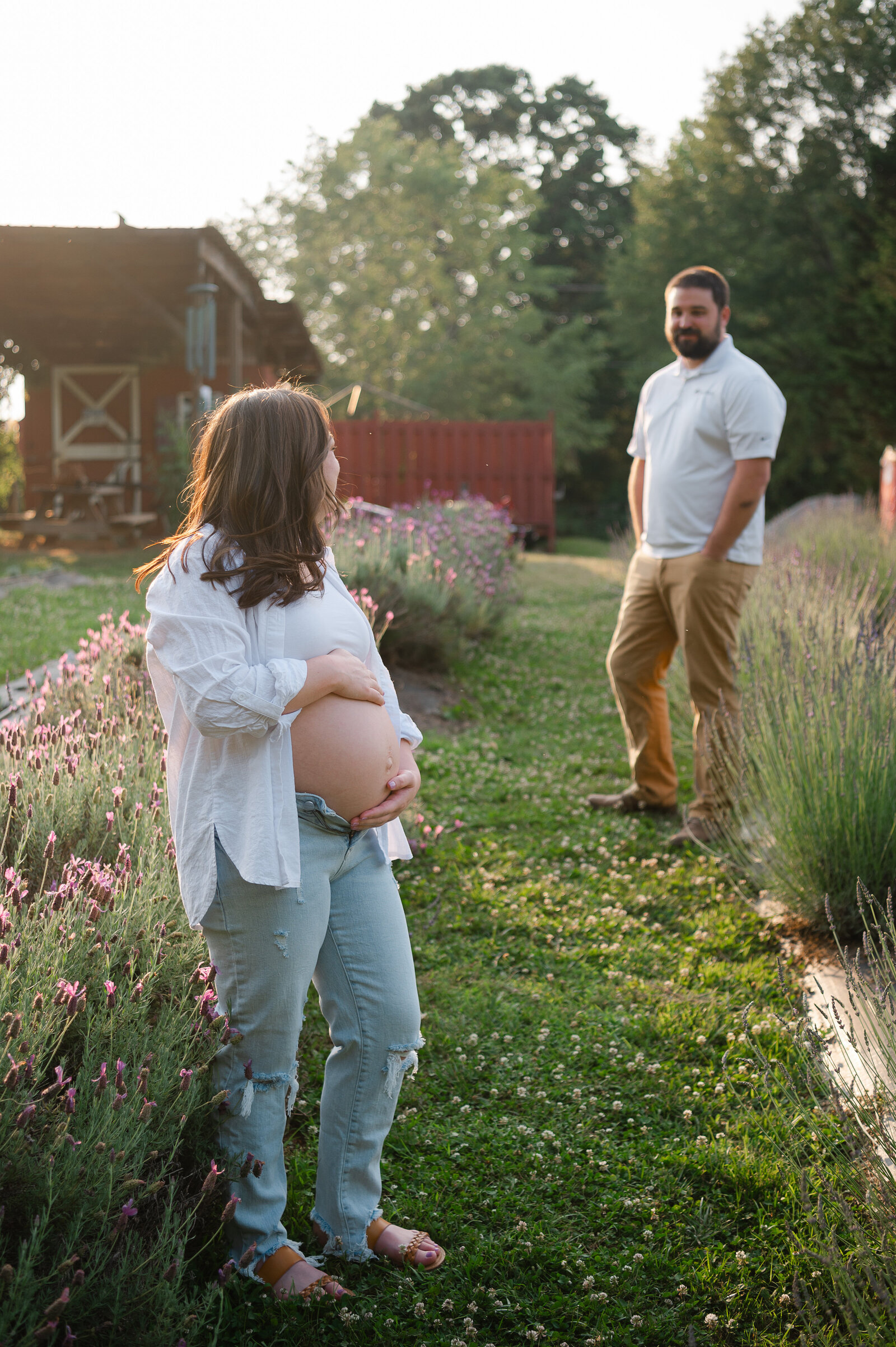 Expecting mother holds her pregnant belly while looking back at her husband in the lavender field located in Dahlonega, Georgia