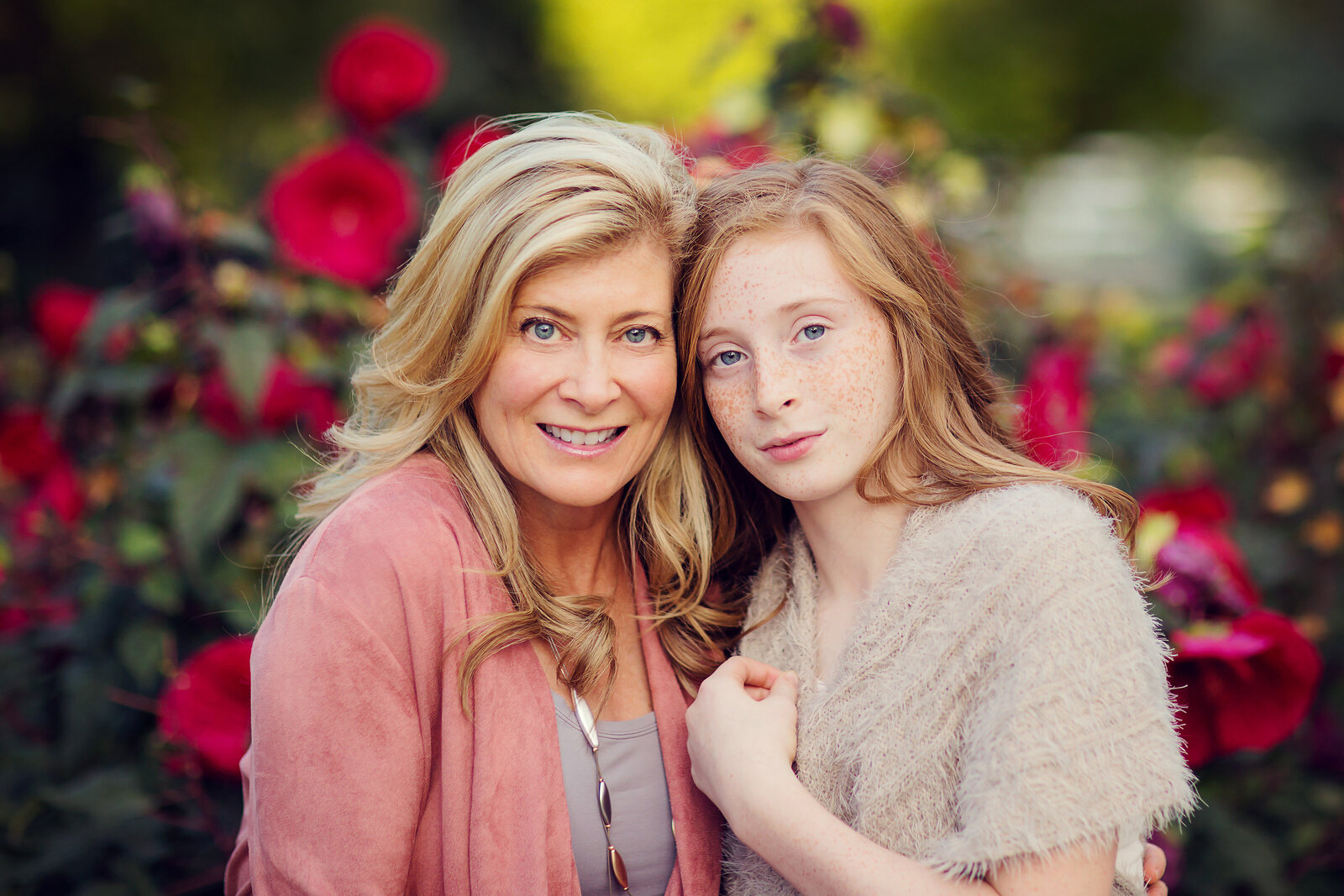 Nice portrait of mom and her teenage daughter at their home. They have gorgeous dark pink flowers behind them.