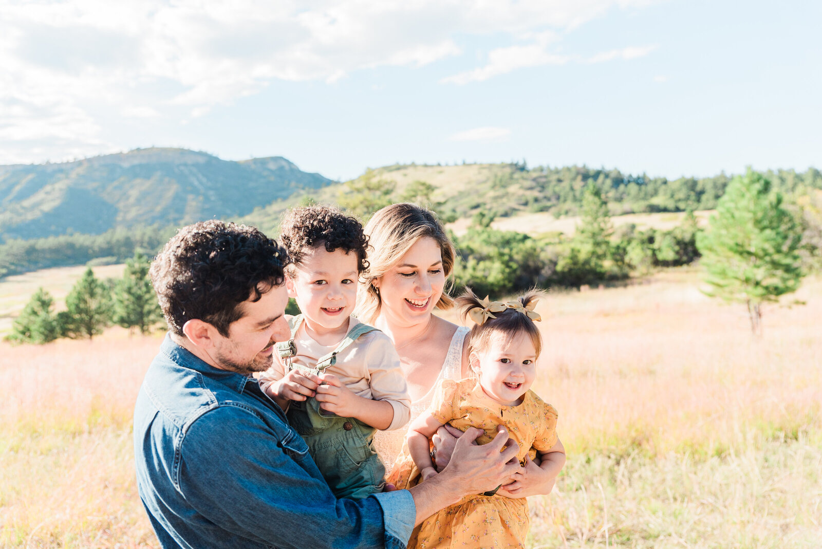 A family with 2 little ones interacts with each other while holding the kids in the parent's arms captured by denver family photographer