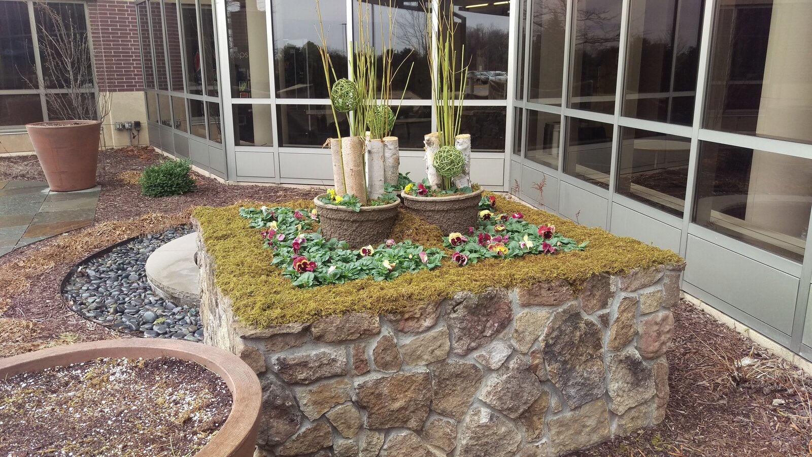 commercial flower bed with 2 tall pots in center surroudned by flowers and moss