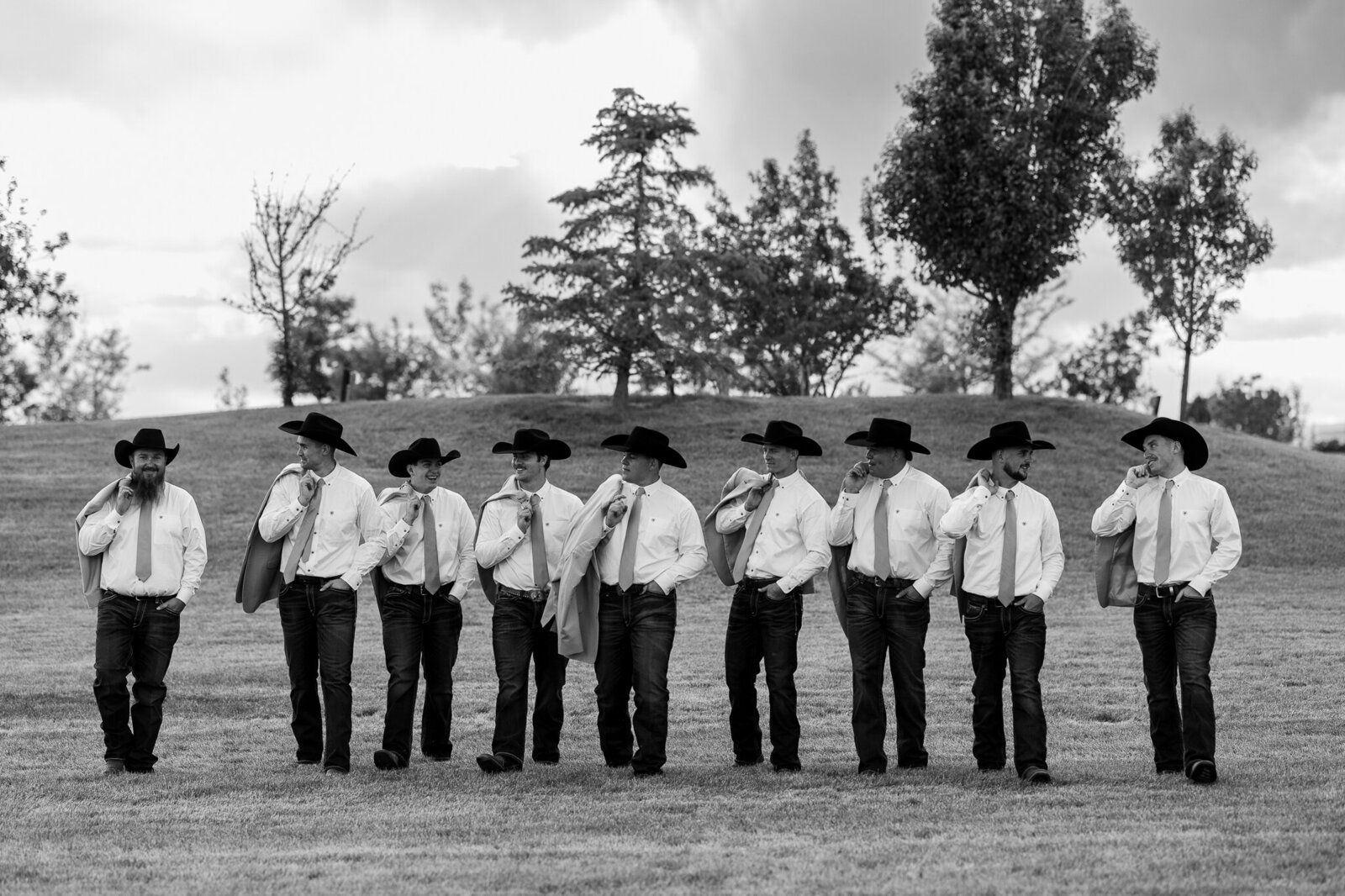 Black and white photo of groomsmen walking with jackets thrown over their shoulders at a Loma, Colorado wedding