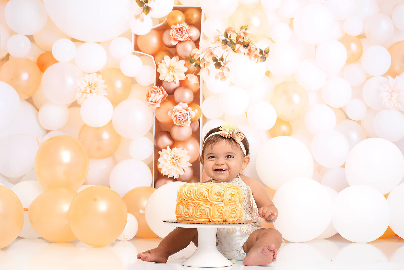 girl smiles directly behind a peach rosette style cake, with a large 1 behind her made from peach and white flowers