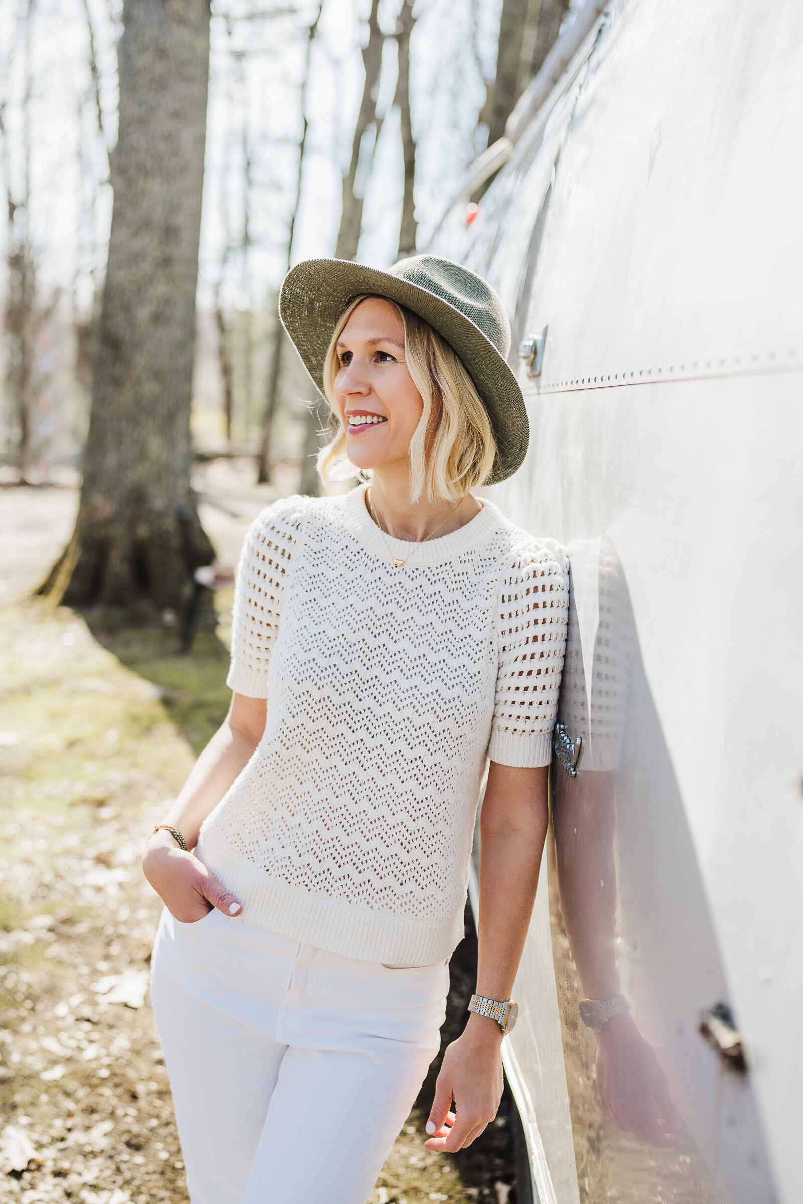 woman leans against airstream in boho hat