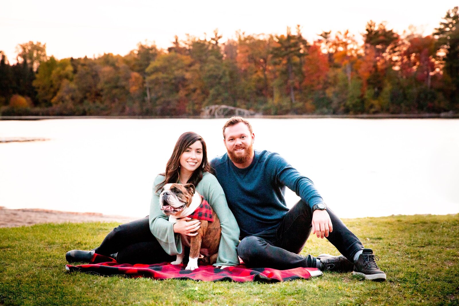 Couple pose with their dog in front of Pinehurst Lake during the fall.