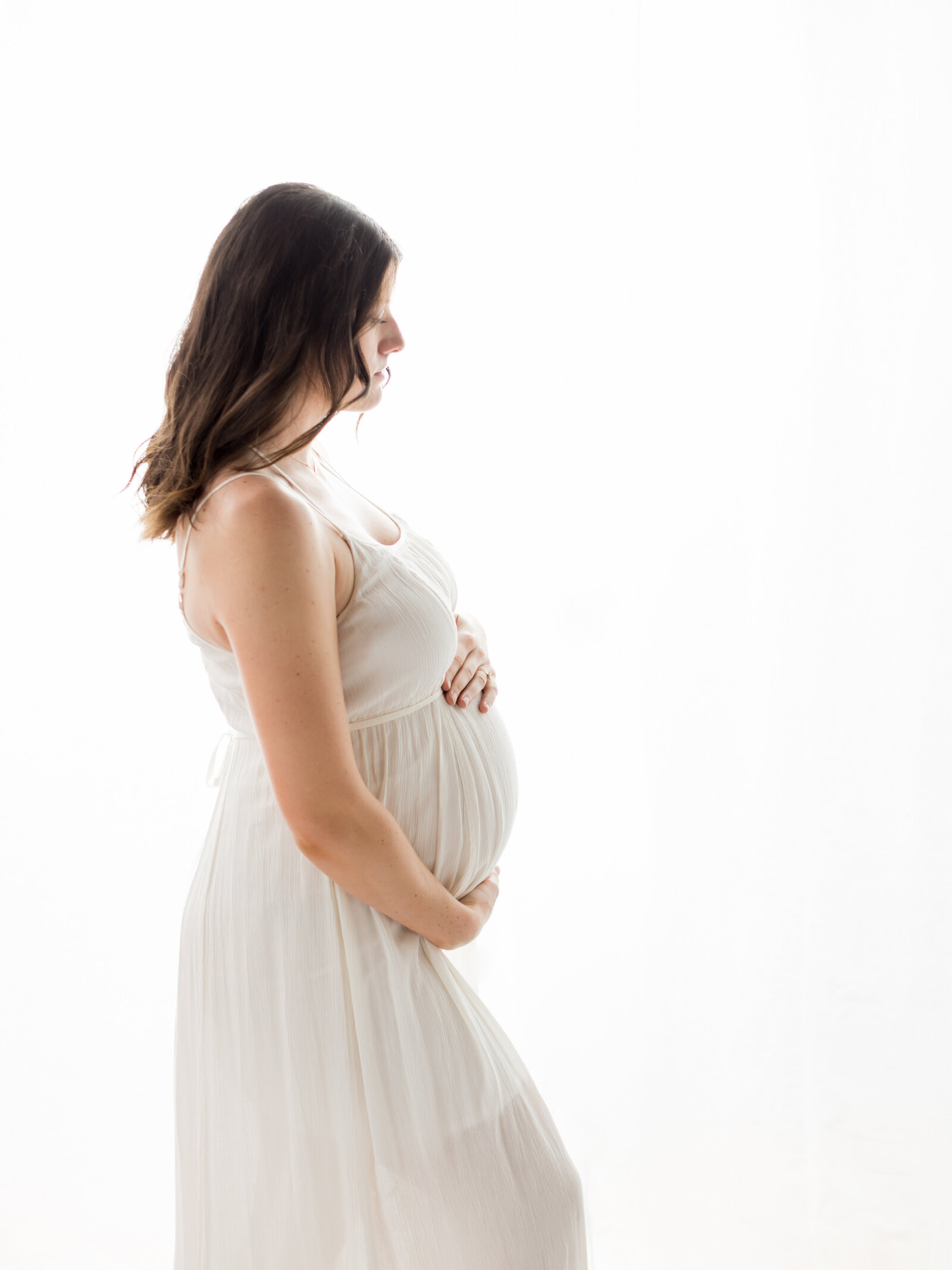 pregnant mom holding belly wearing white boho dress for maternity photoshoot