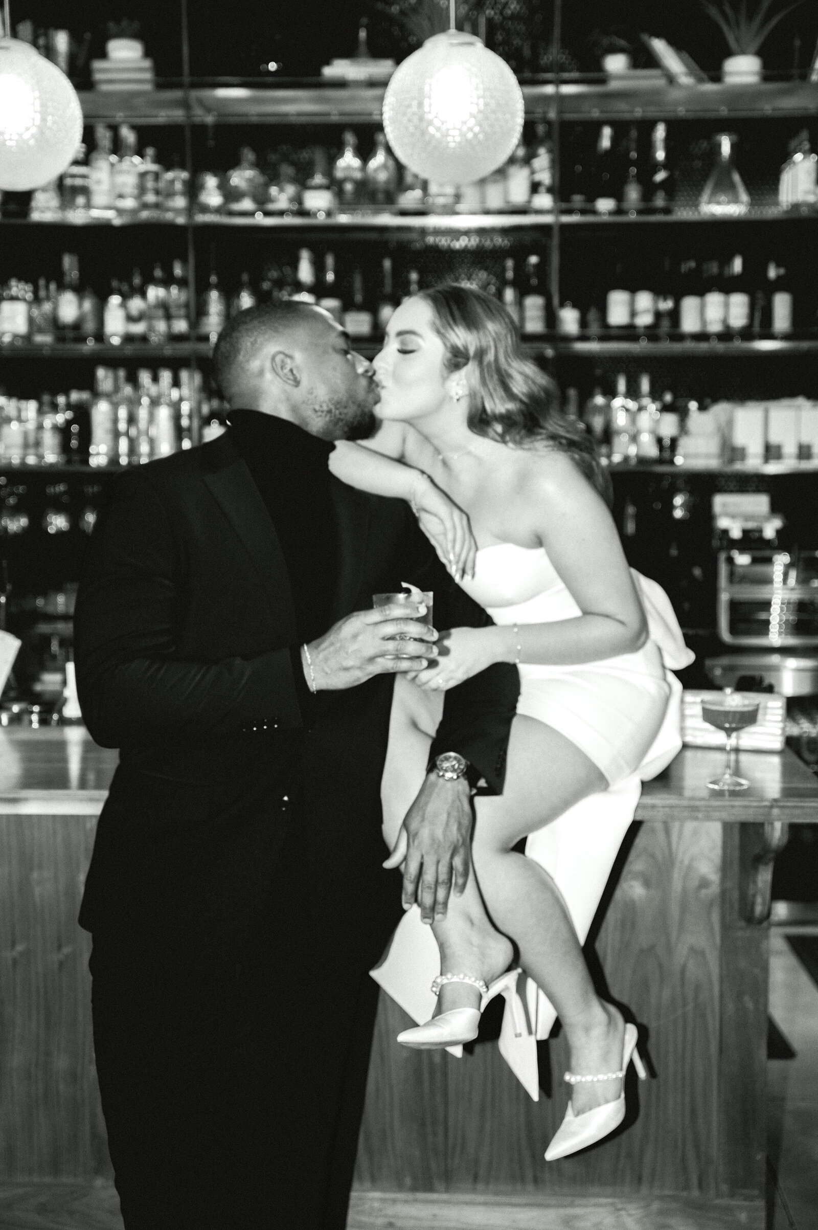 classy modern direct flash engagement photo of couple at a bar kissing. black and white photo of woman sitting on the bar kissing a man at austin engagement photo
