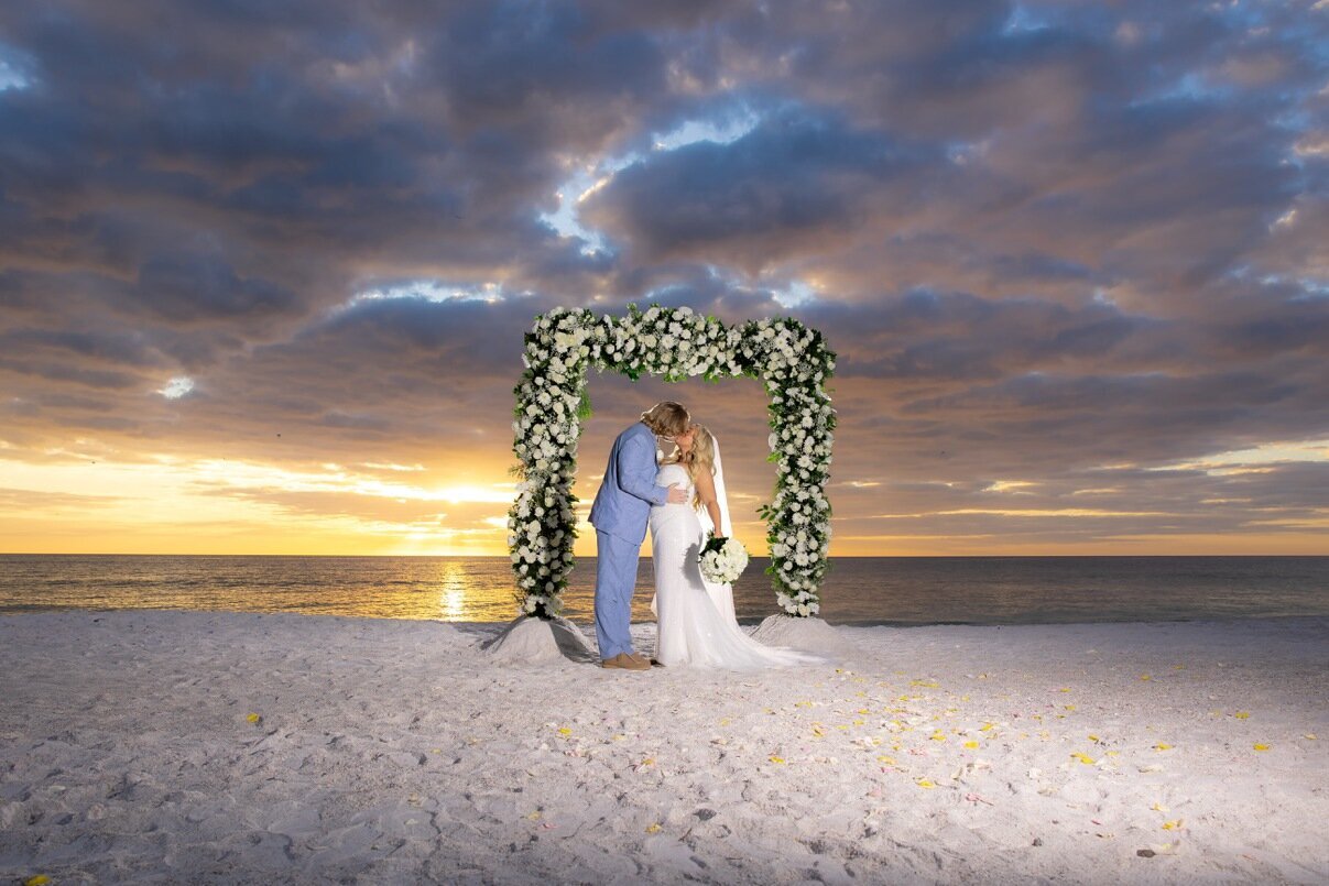 Beautiful bride and groom kissing under a flower archway by Sarasota wedding photographer, Love and Style Photography