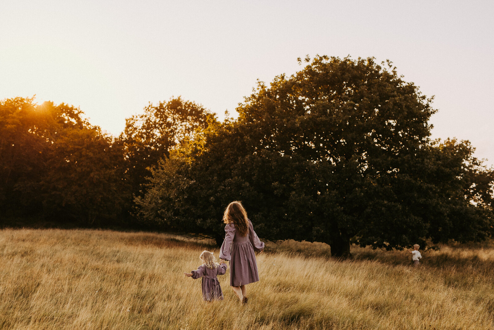 en mamma och hennes dotter går hand i hand på ett fält i solnedgånngen under deras familjefotografering