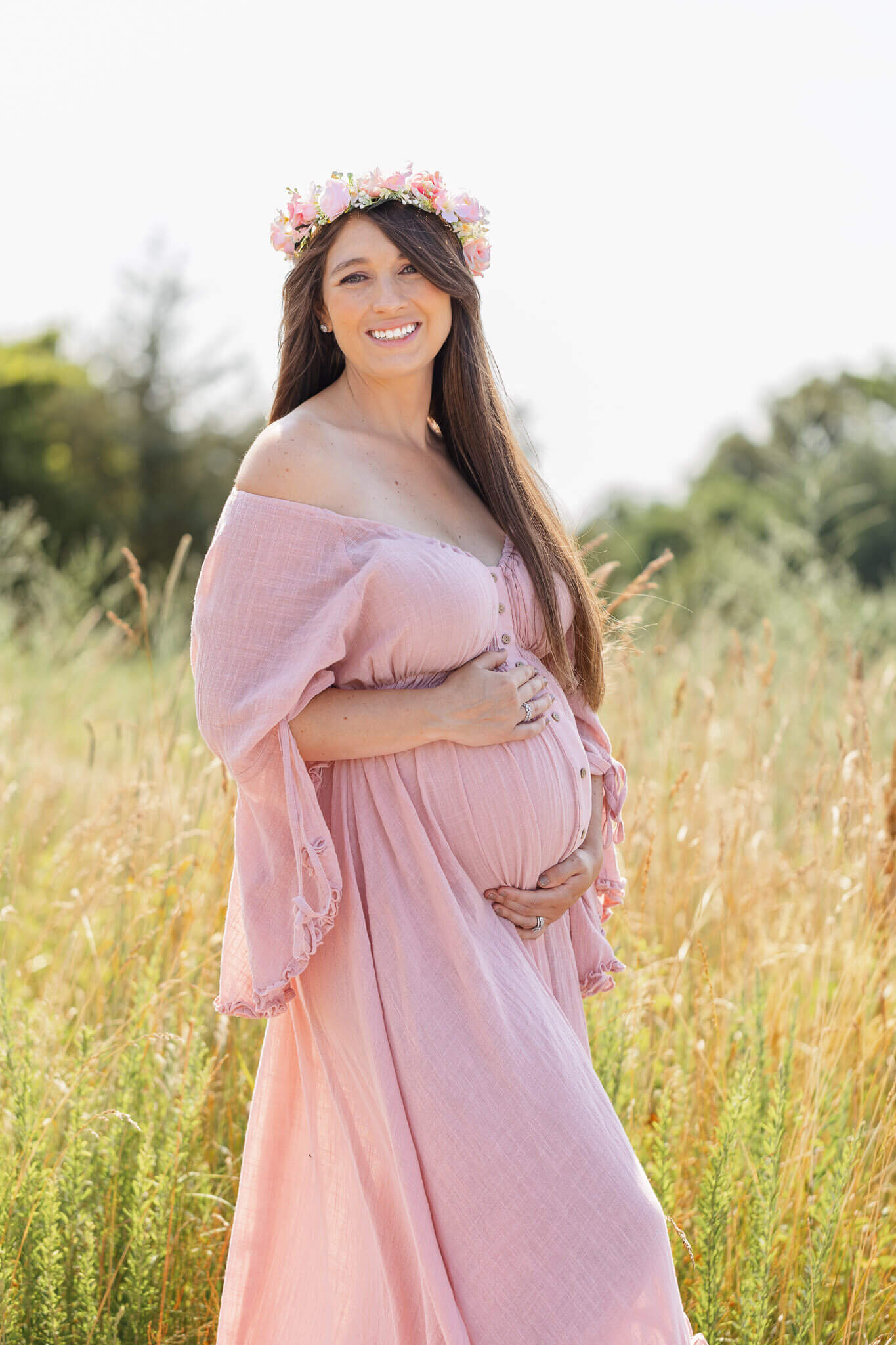 An expecting woman posing in a pink dress in front of tall grass in Northern Virginia.