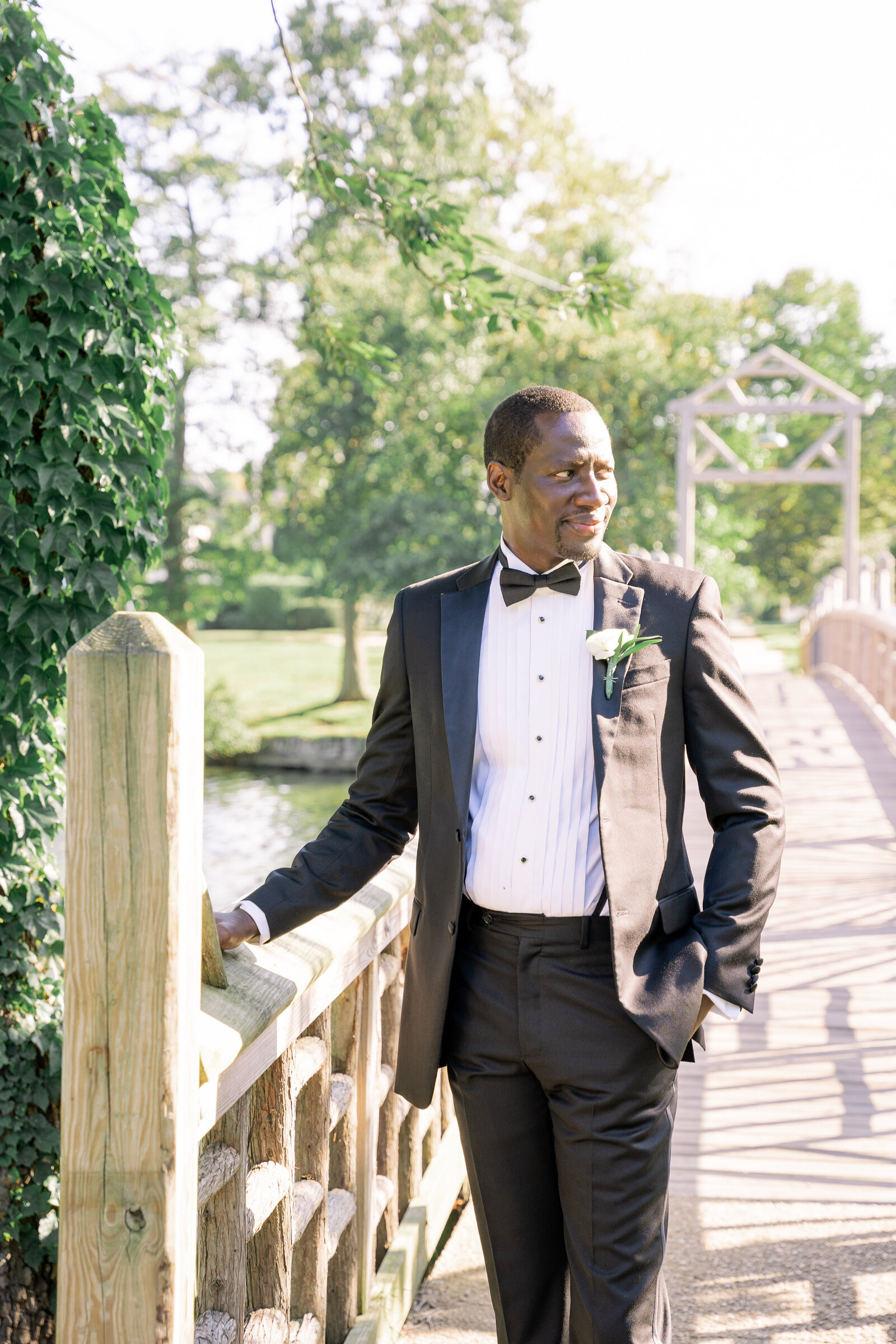 african american groom next to bridge in tuxedo bride holding veil and bouquet by bridge Divine Park Spring Lake NJ