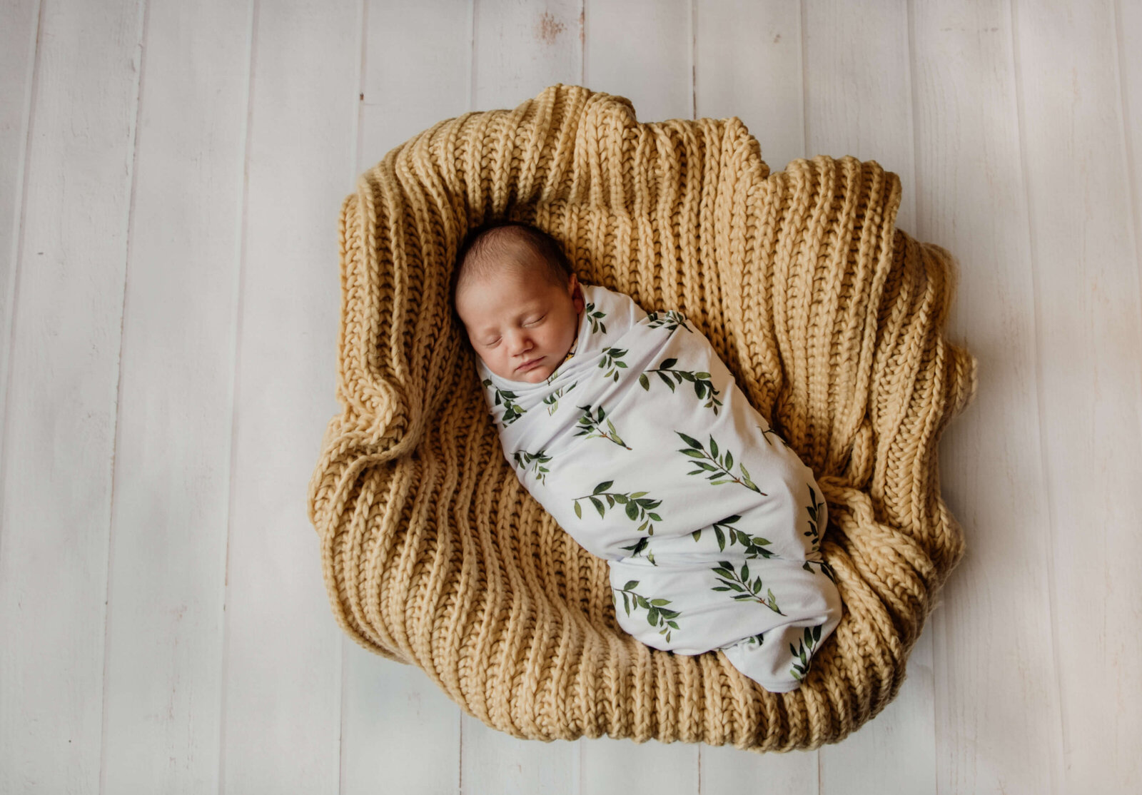 Baby in a basket on white wood floor.