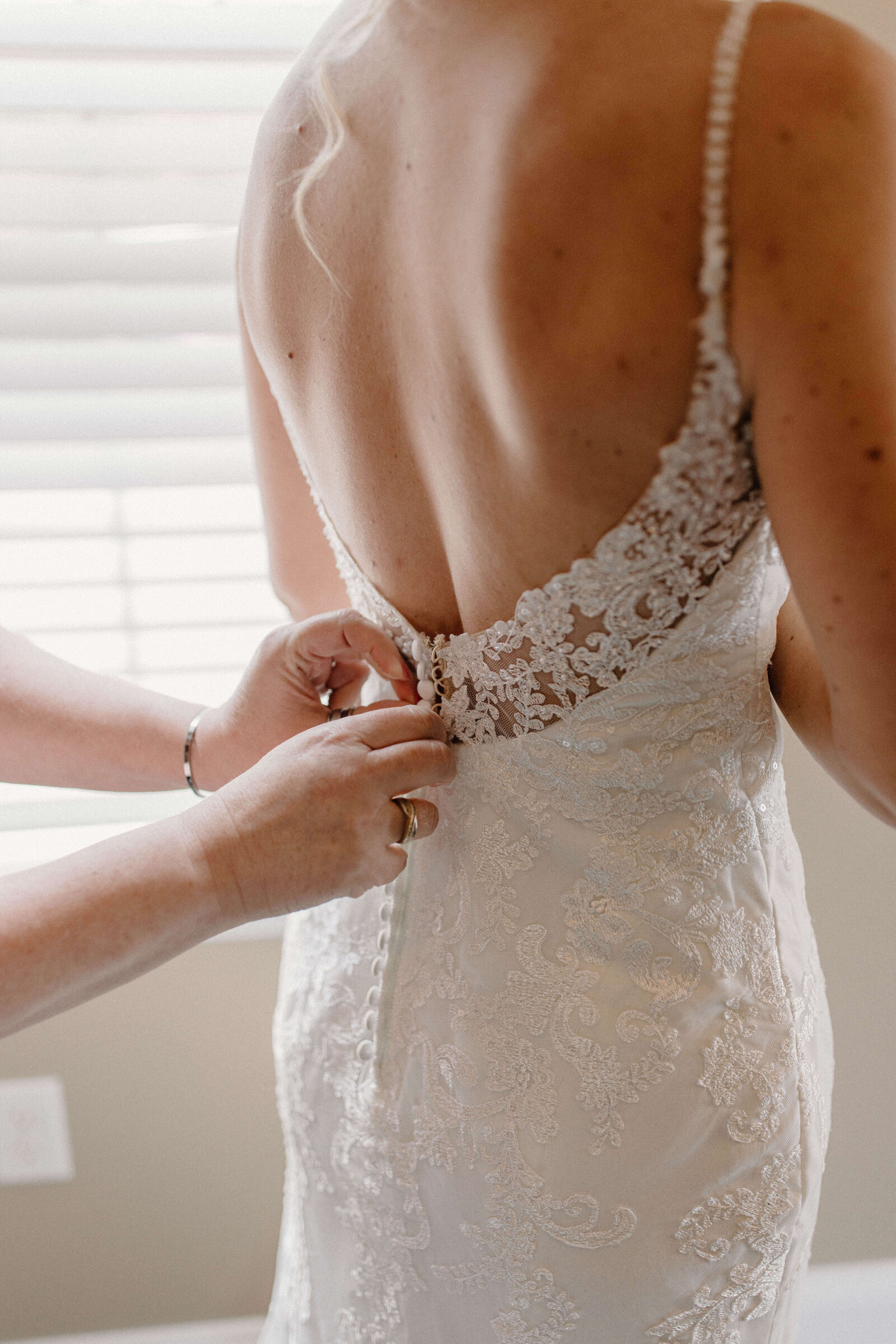 MOH buttoning up brides dress in getting ready suite by delaware wedding photographer sabrina leigh