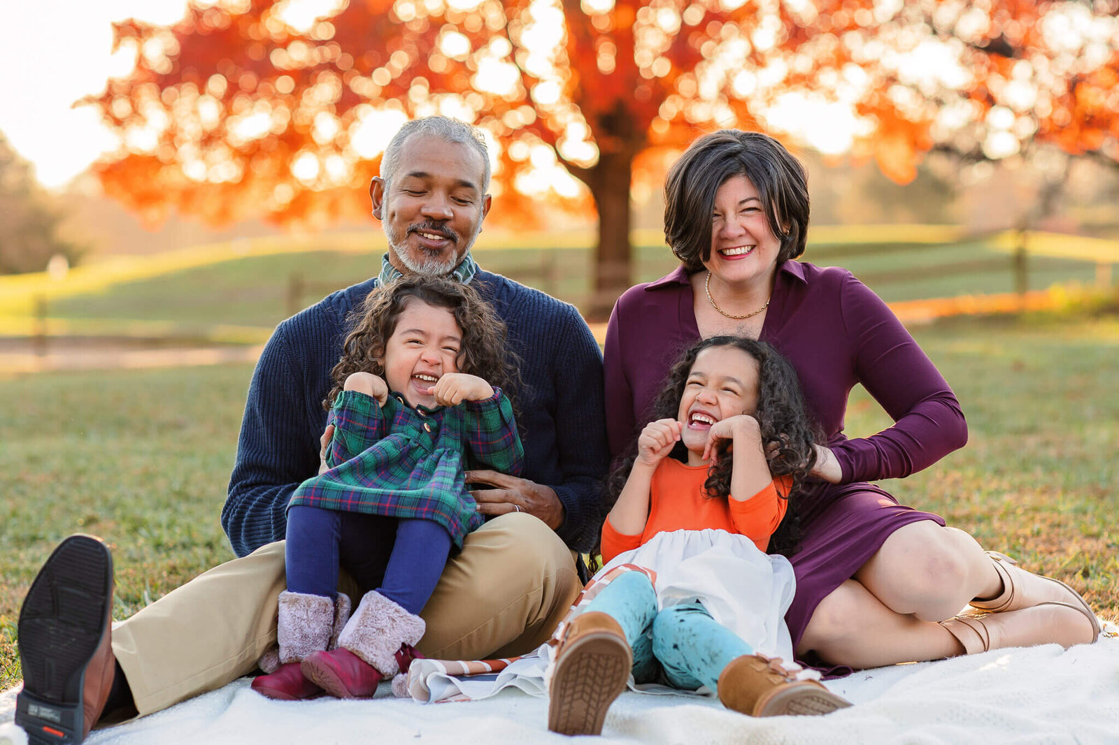 A family sitting on a blanket and having a tickle fight