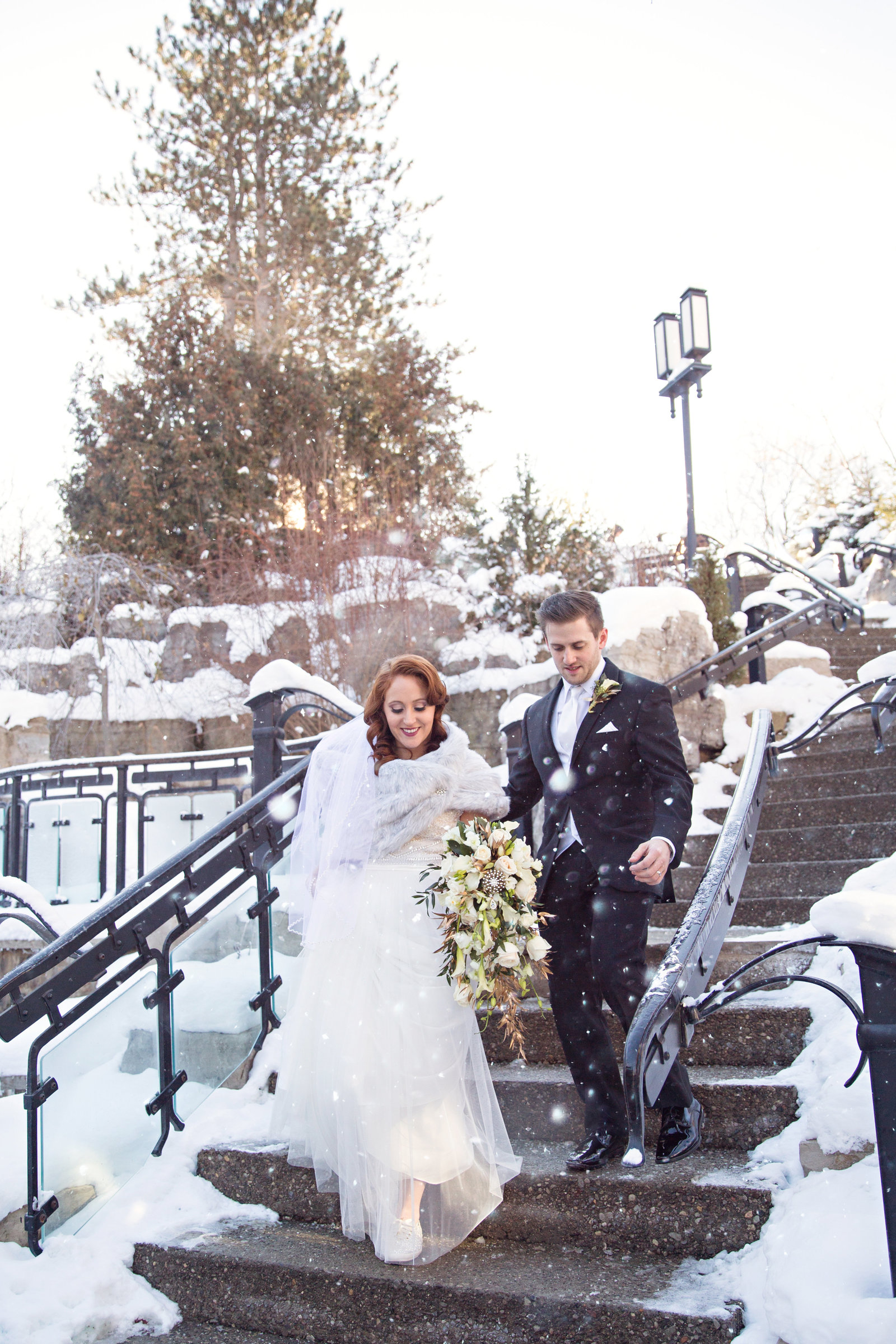 winter bride and groom walking down snowy stairs at Ancaster Mill