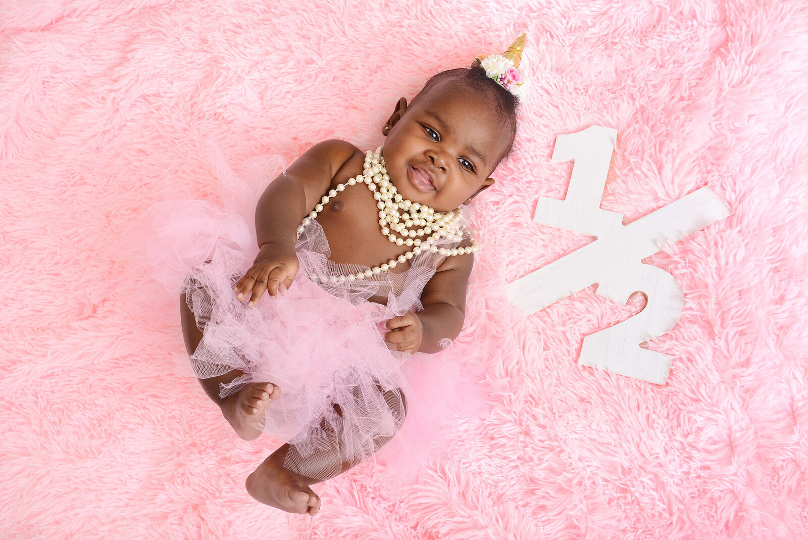 girl lays down on a pink blanket at a half birthday photoshoot