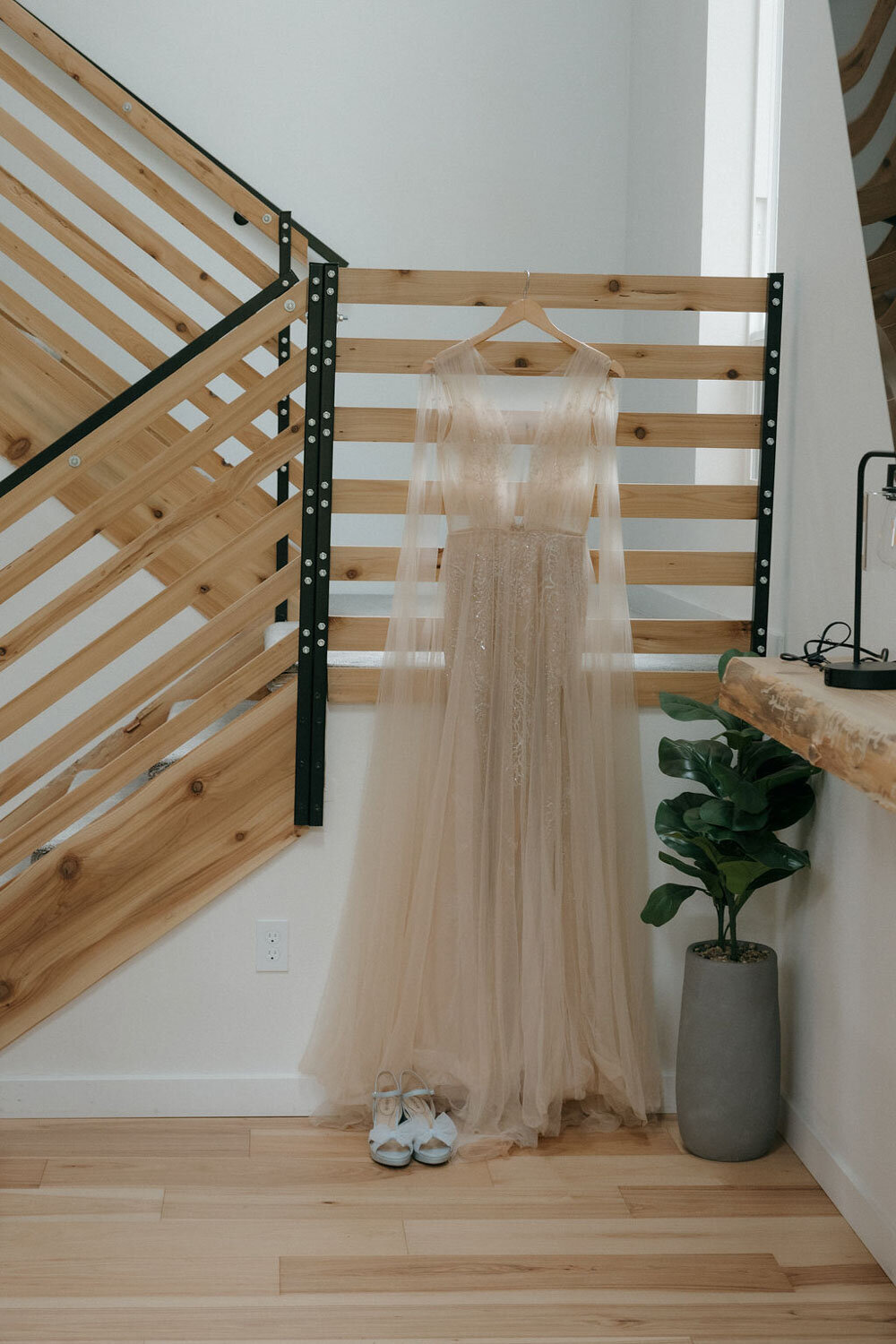 Flowing blush wedding gown hanging beside a wooden staircase