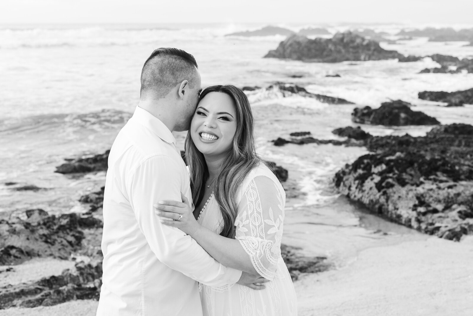 An engaged man and woman take photos on the beach in Pacific Grove, Monterey, California near Big Sur.