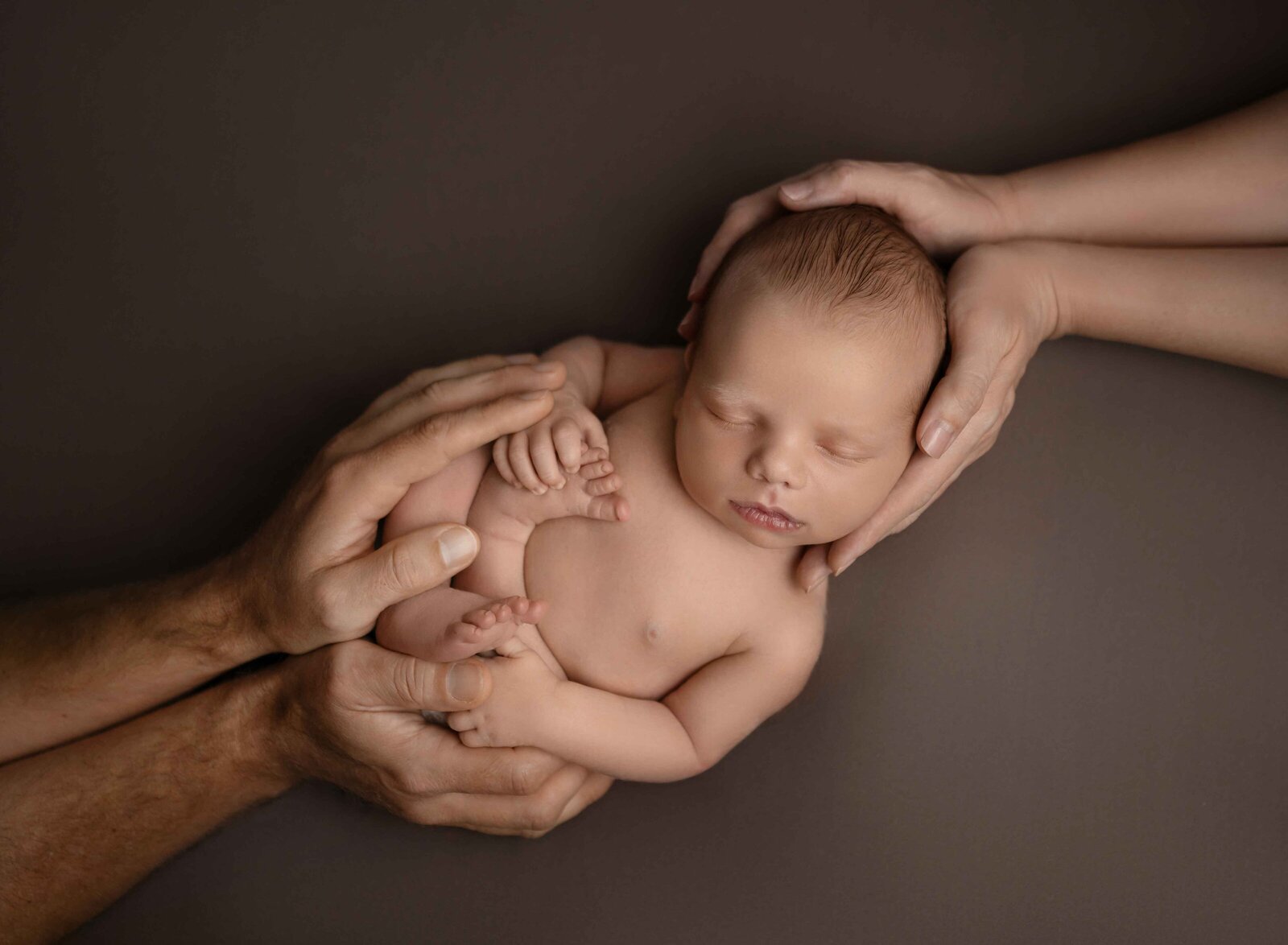 Baby sleeping with Mom cradling head and Dad cradling legs.