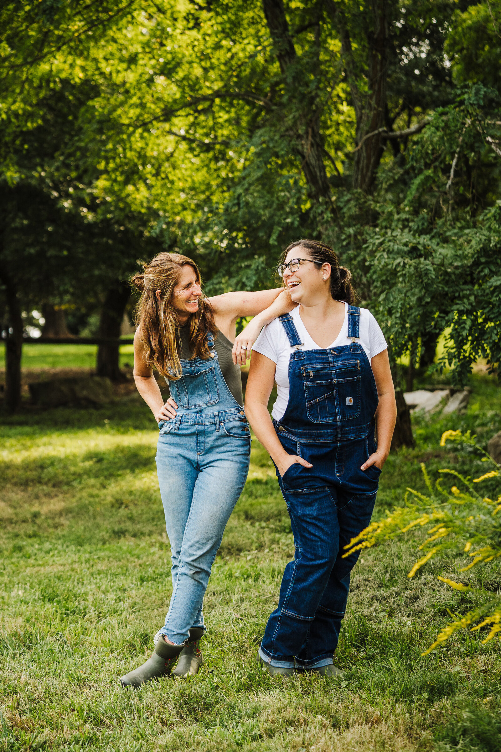 two gardeners in overalls laugh together outdoors