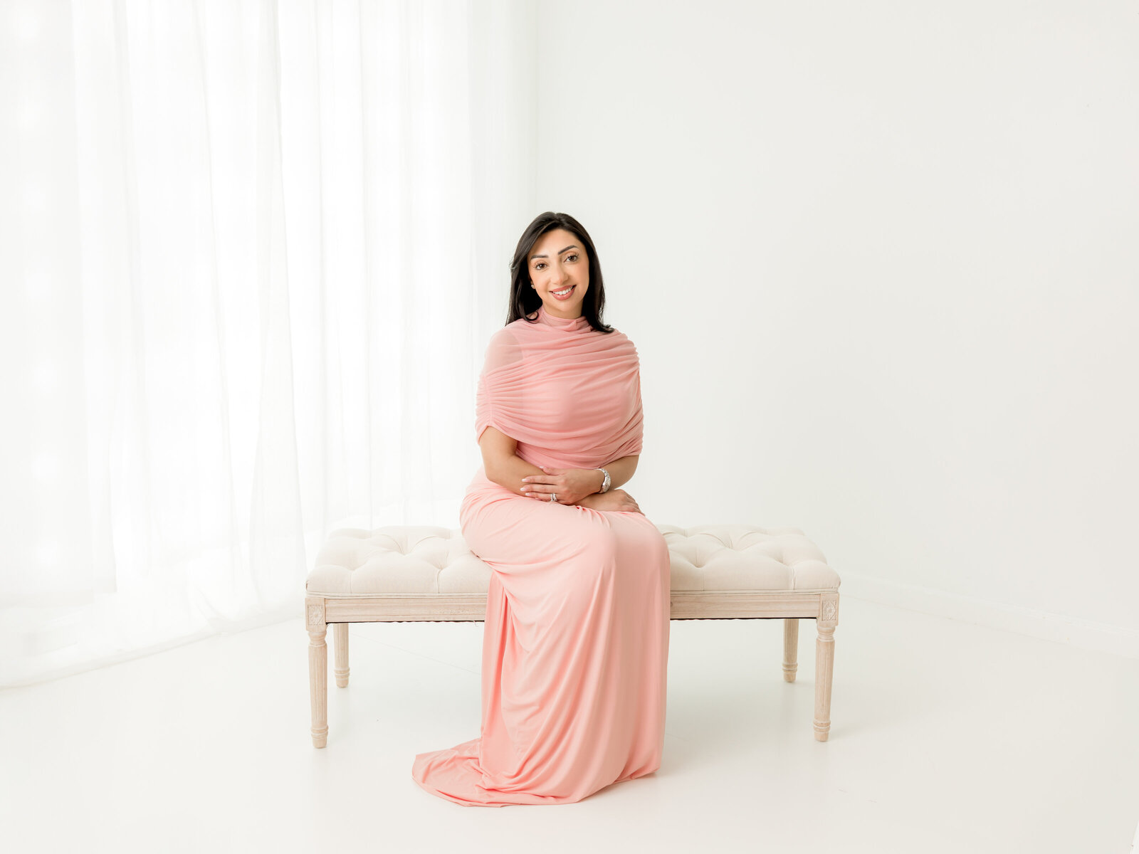 women in pink dress sitting on bench for white studio portrait