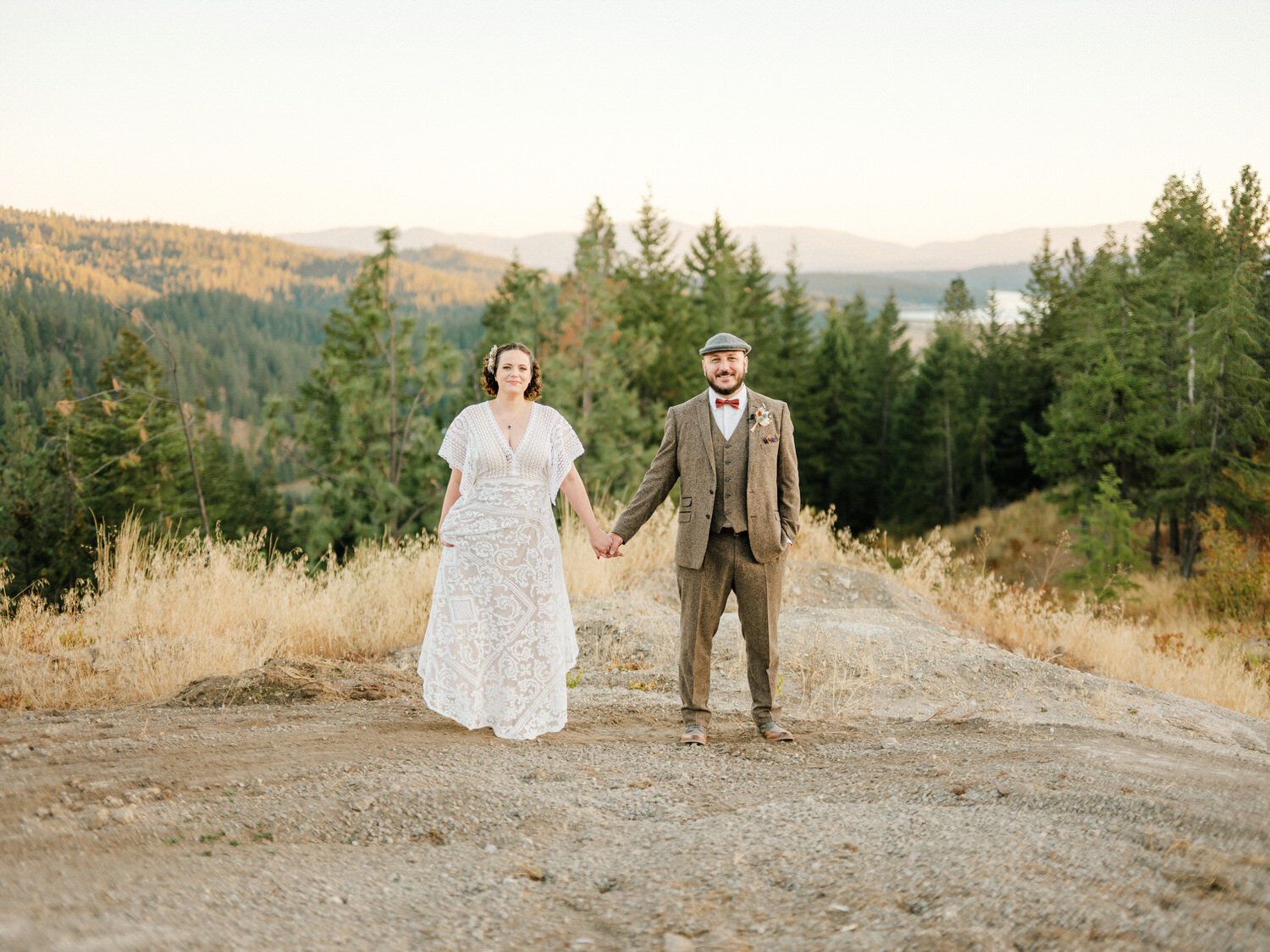 Bride and groom hold hands while standing on a hill