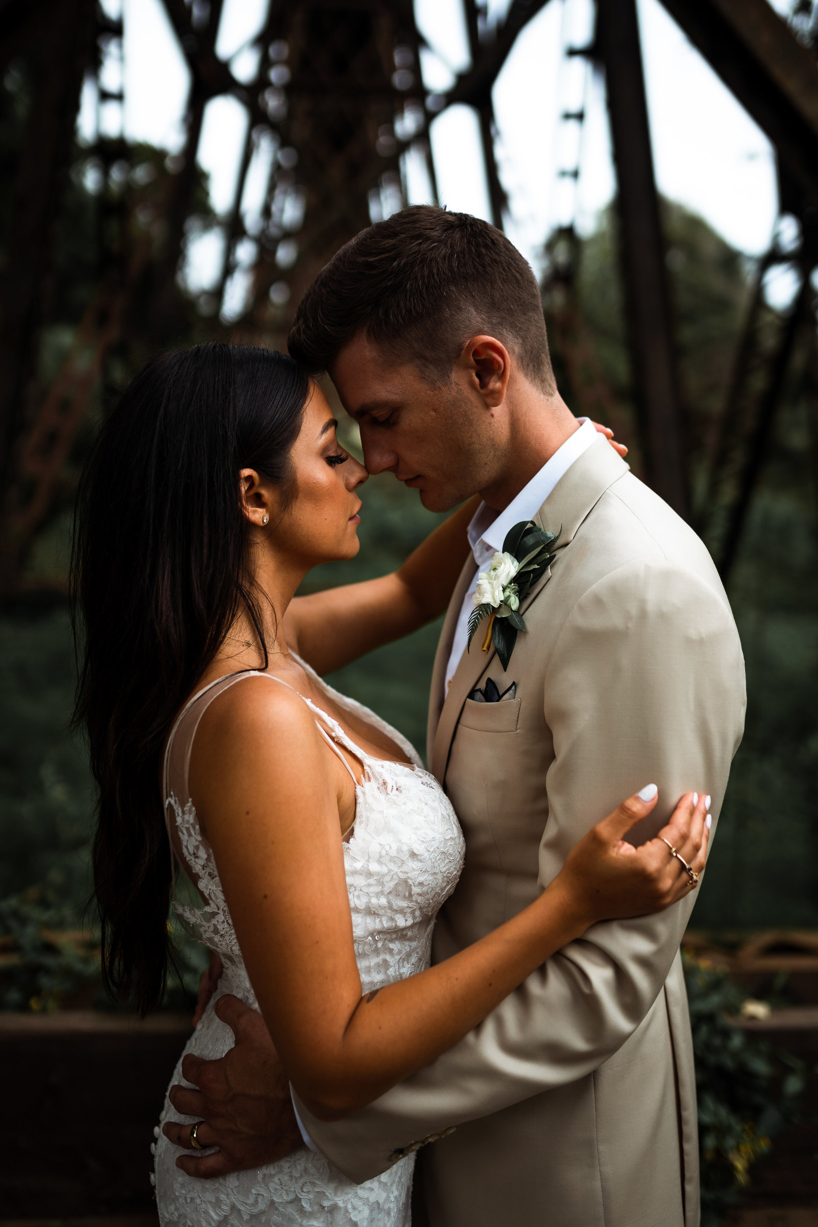 Wedding couple holding each other very intimately, with noses touching and eyes closed with serious facial expressions.