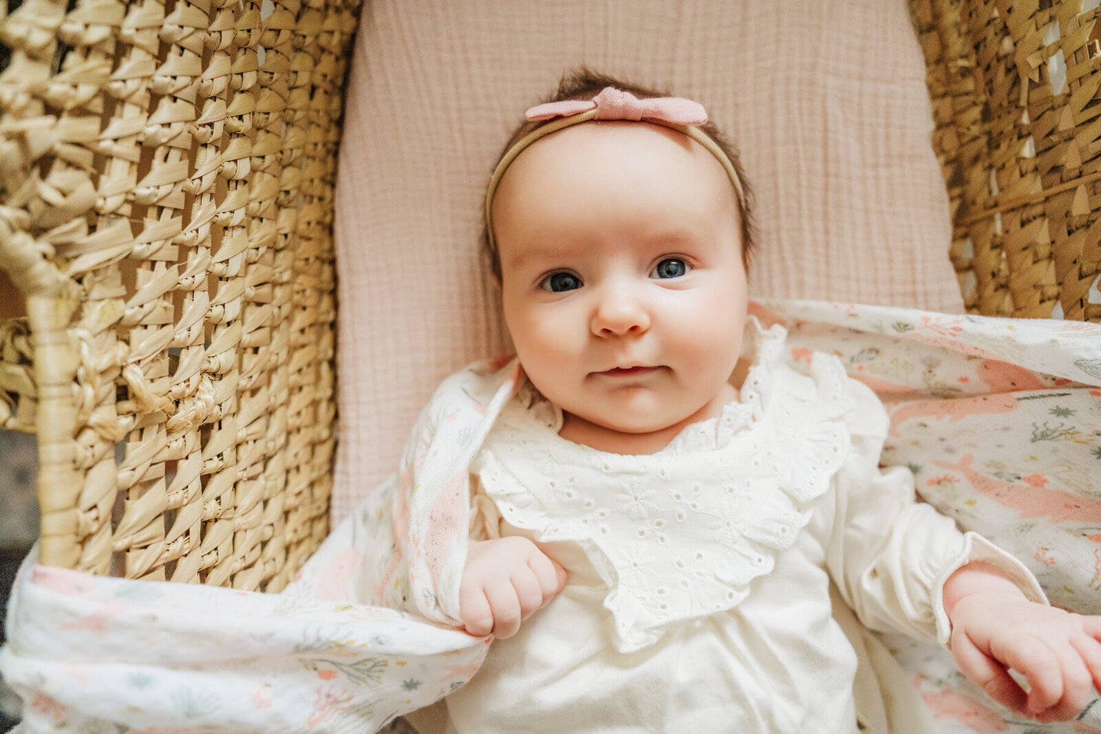 newborn girl stares at camera from a wicker bassinet